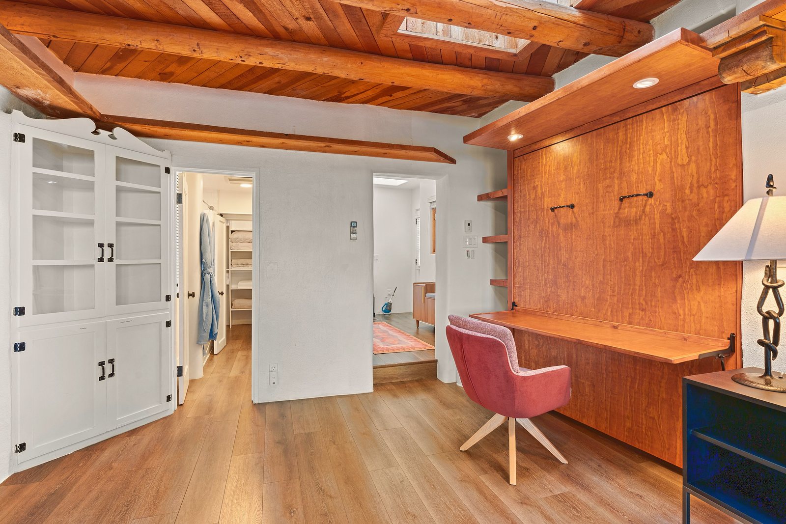 The casita's bed folded up into a wall of warm custom wood, the desk surface down and a chair pulled up, under vigas and a skylight.