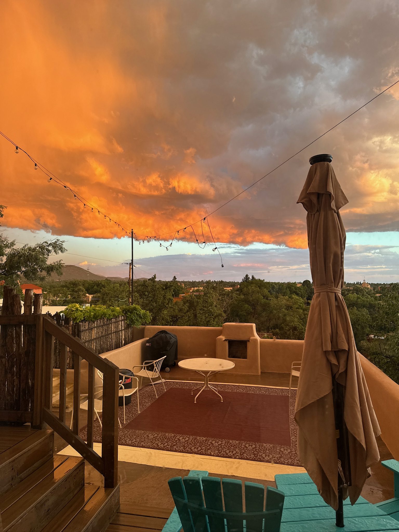 Sunset from the deck with the whole sky gone orange, the umbrella furled and the turquoise chairs in silhouette against it.