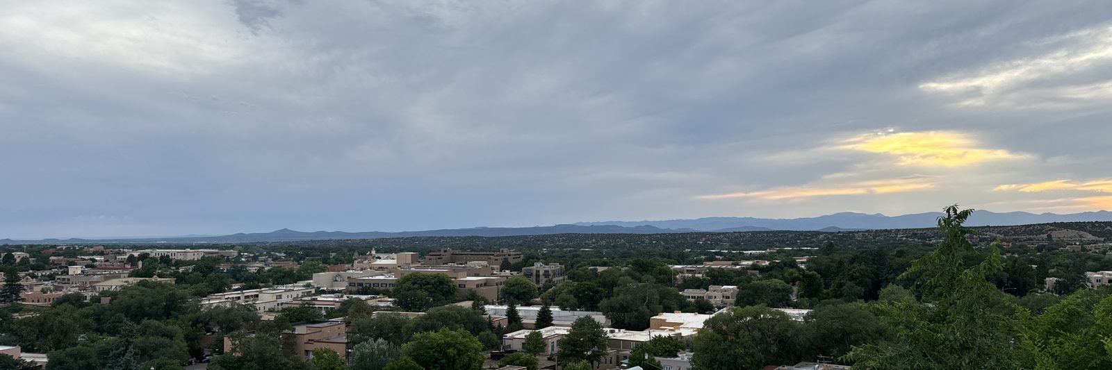 Dusk over Santa Fe from the hill above the property: adobe rooftops and treetops running out to the ridgeline, with the last of the light along the horizon.