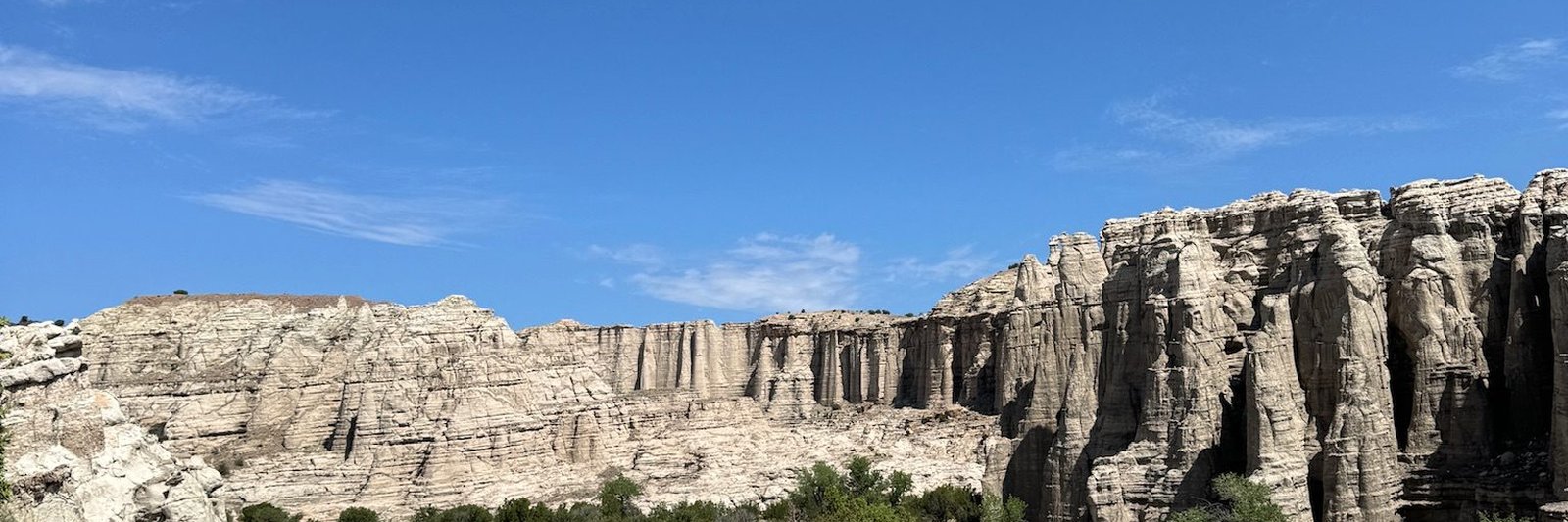 The white rock cliffs at Plaza Blanca standing over green scrub under a deep blue sky.