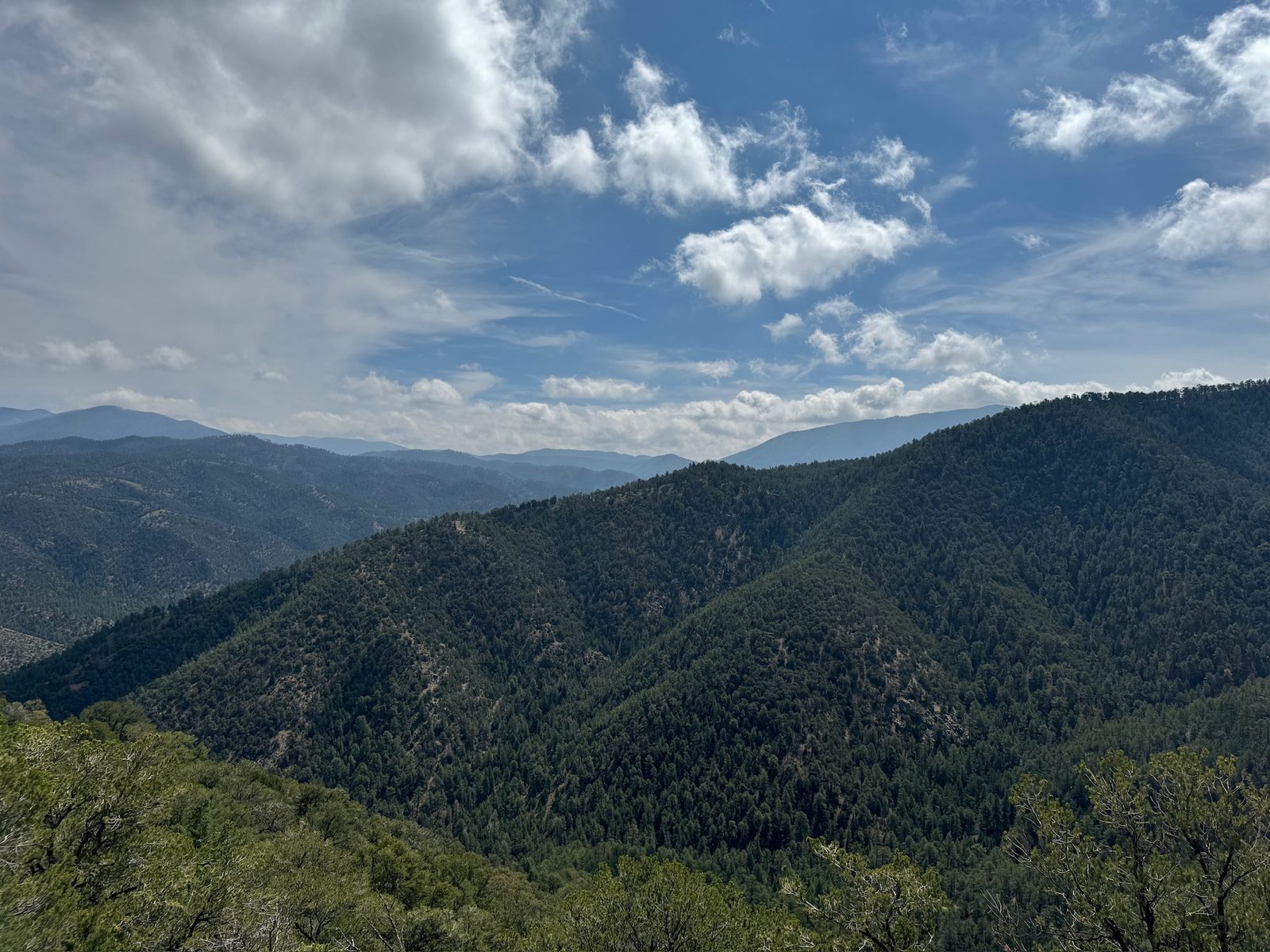 The Sangre de Cristo foothills under a tall sky of broken cloud, ridge after forested ridge running back toward the high peaks.