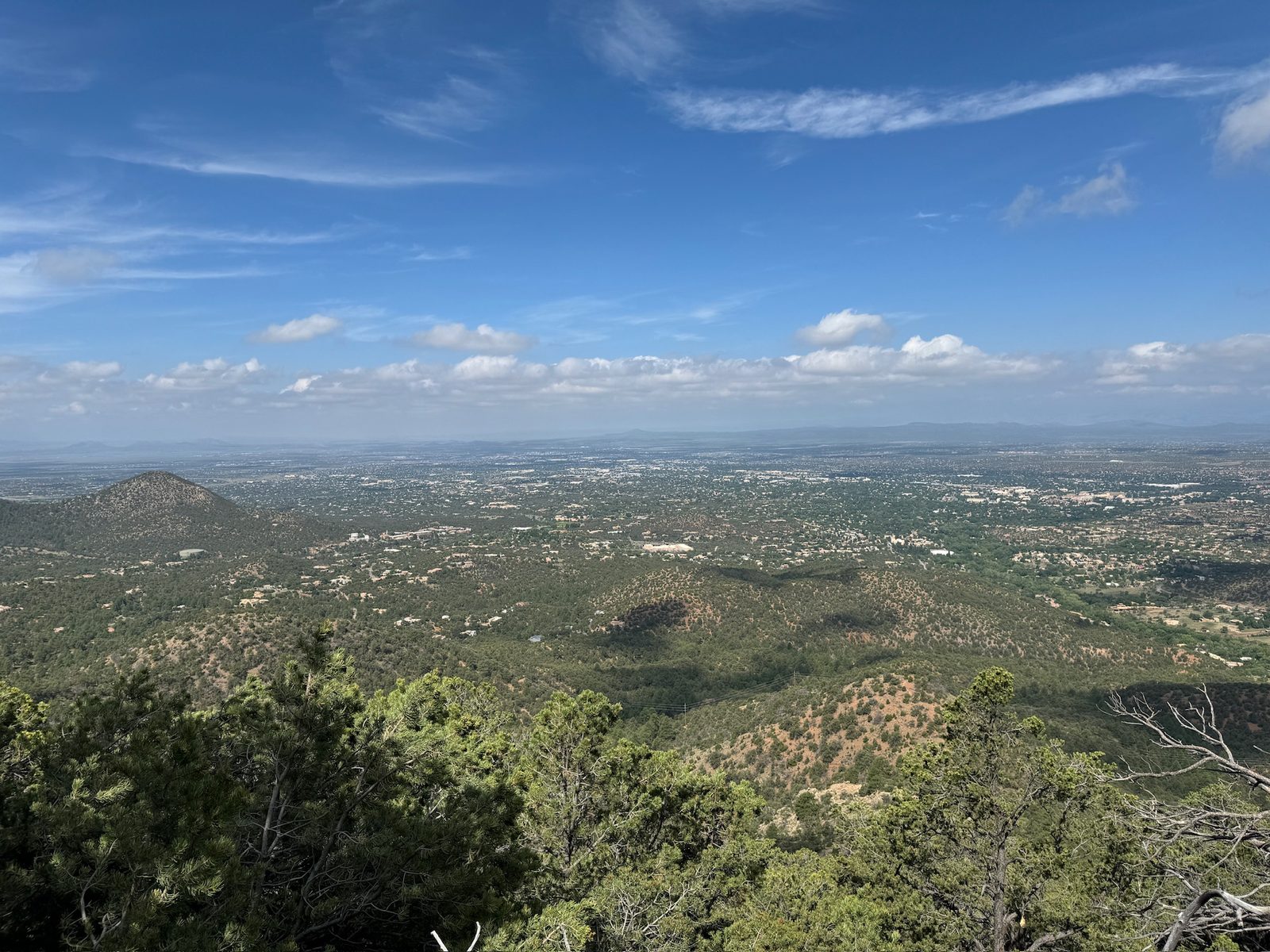 The whole of Santa Fe spread out below the summit, Sun Mountain in the middle distance under a big blue sky.