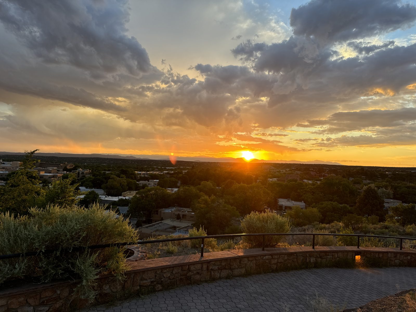 The sun going down over Santa Fe from a stone-walled overlook, cloud lit orange and gold across the whole width of the sky.