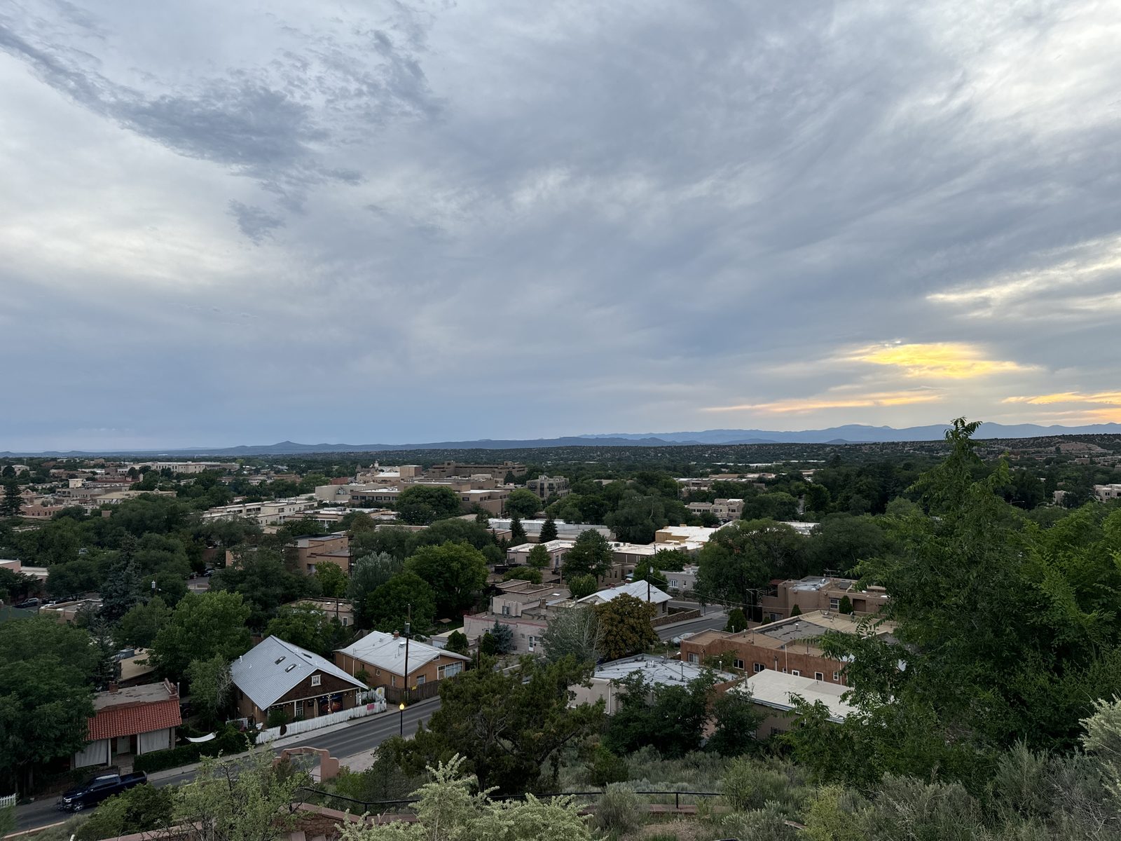 Downtown Santa Fe from the hill at dusk: adobe rooftops in the trees, the last gold light on the horizon under a big grey sky.