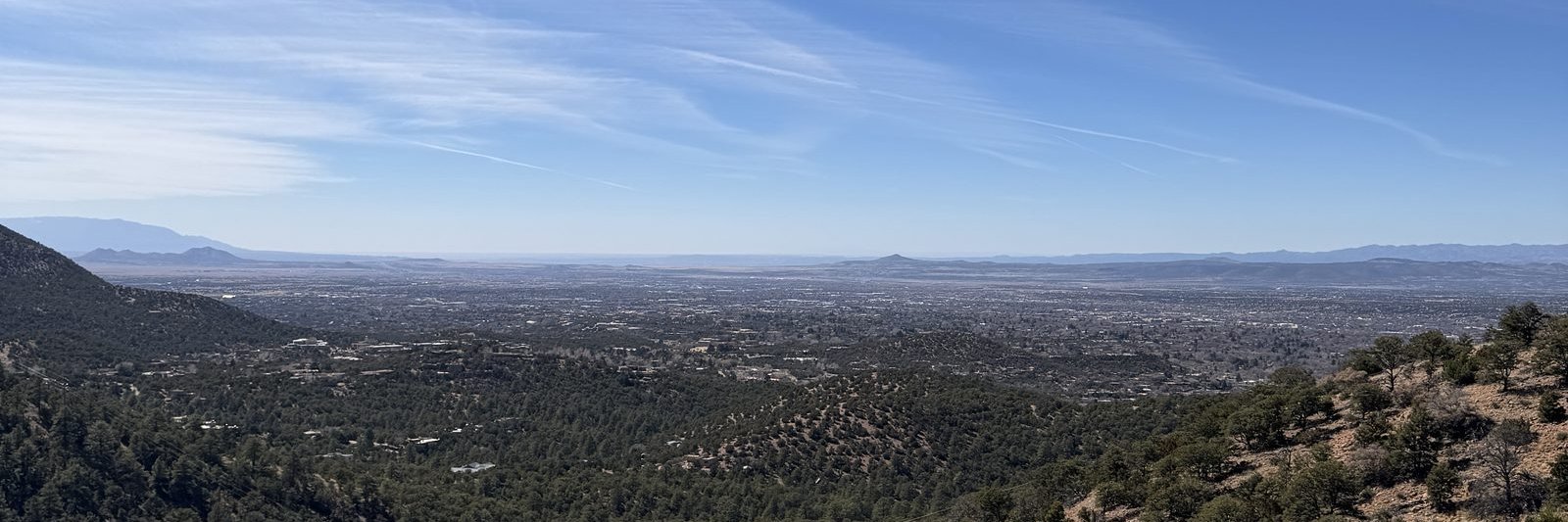 The whole Santa Fe valley from a granite outcrop on the ridge, pinon and ponderosa falling away to the plain and the far range on the horizon.
