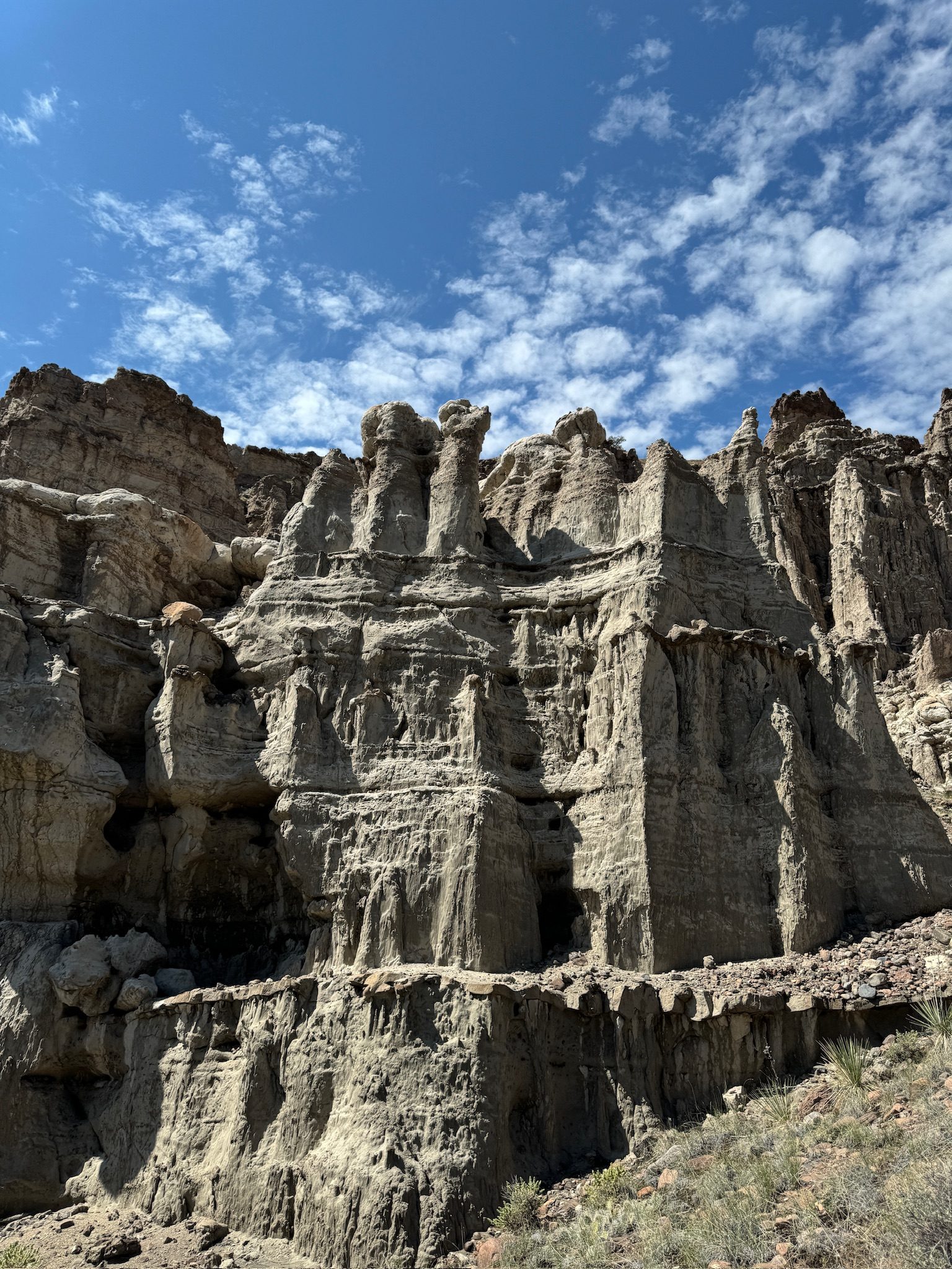 Pale eroded rock towers and cliffs rising against a blue sky of scattered cloud.