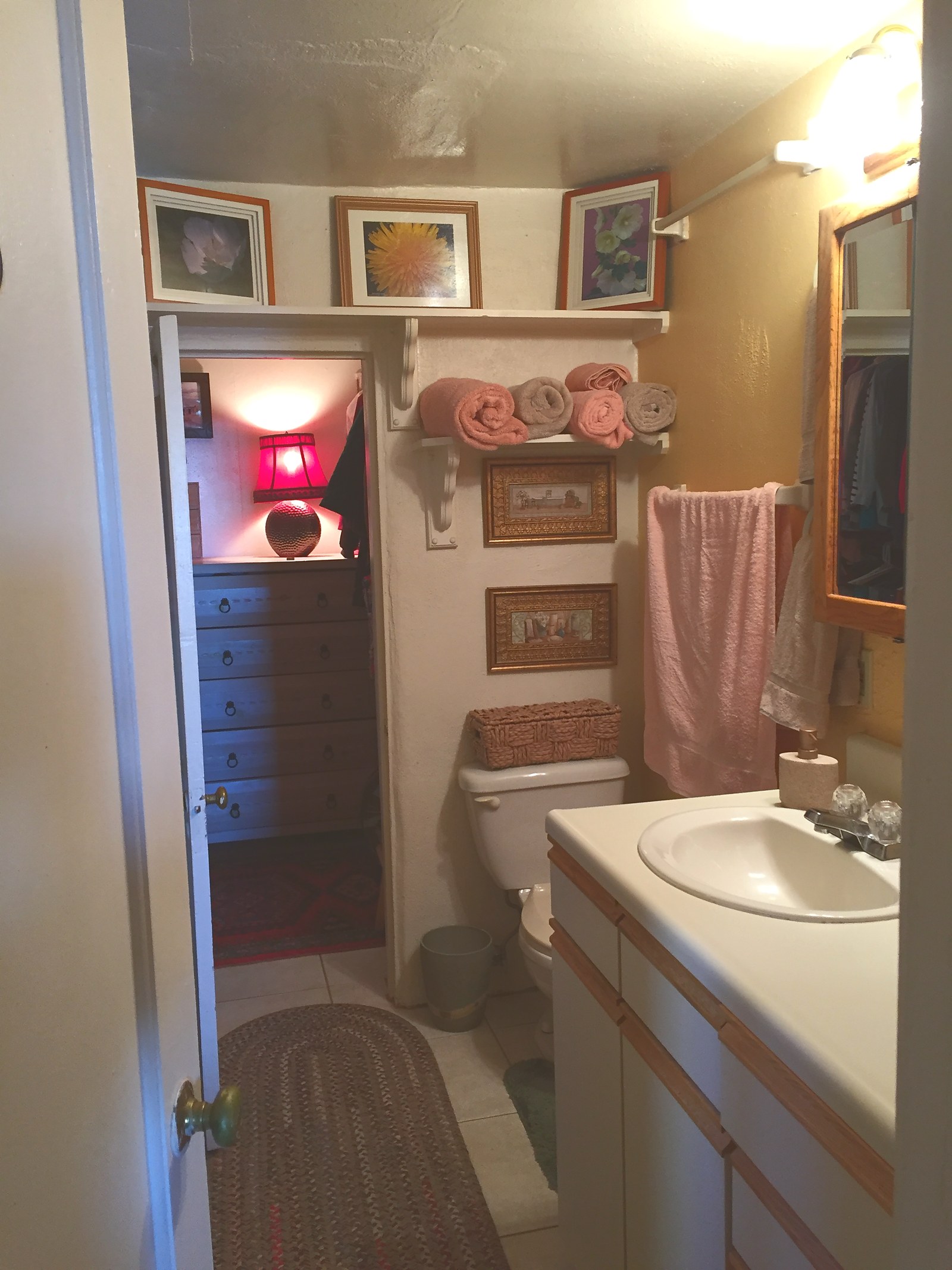 The casita bathroom in 2018: a laminate vanity with a moulded basin, rolled towels on a bracket shelf, small framed prints and a yellow wall.