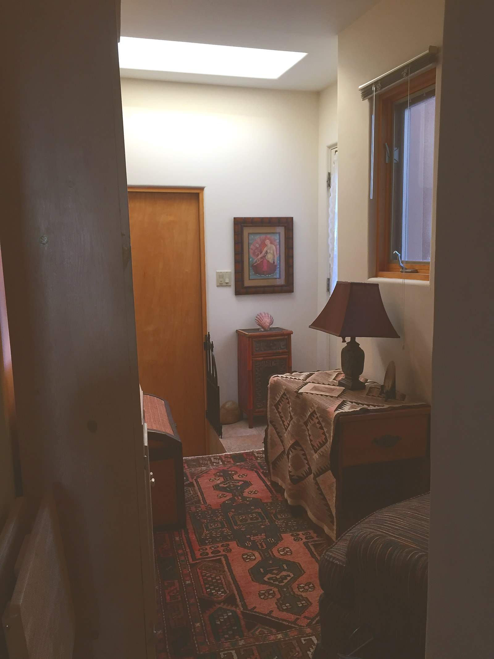 The casita entry in 2018, looking through to a skylit hall with a panelled door, a framed print, a small painted cabinet and a lamp.