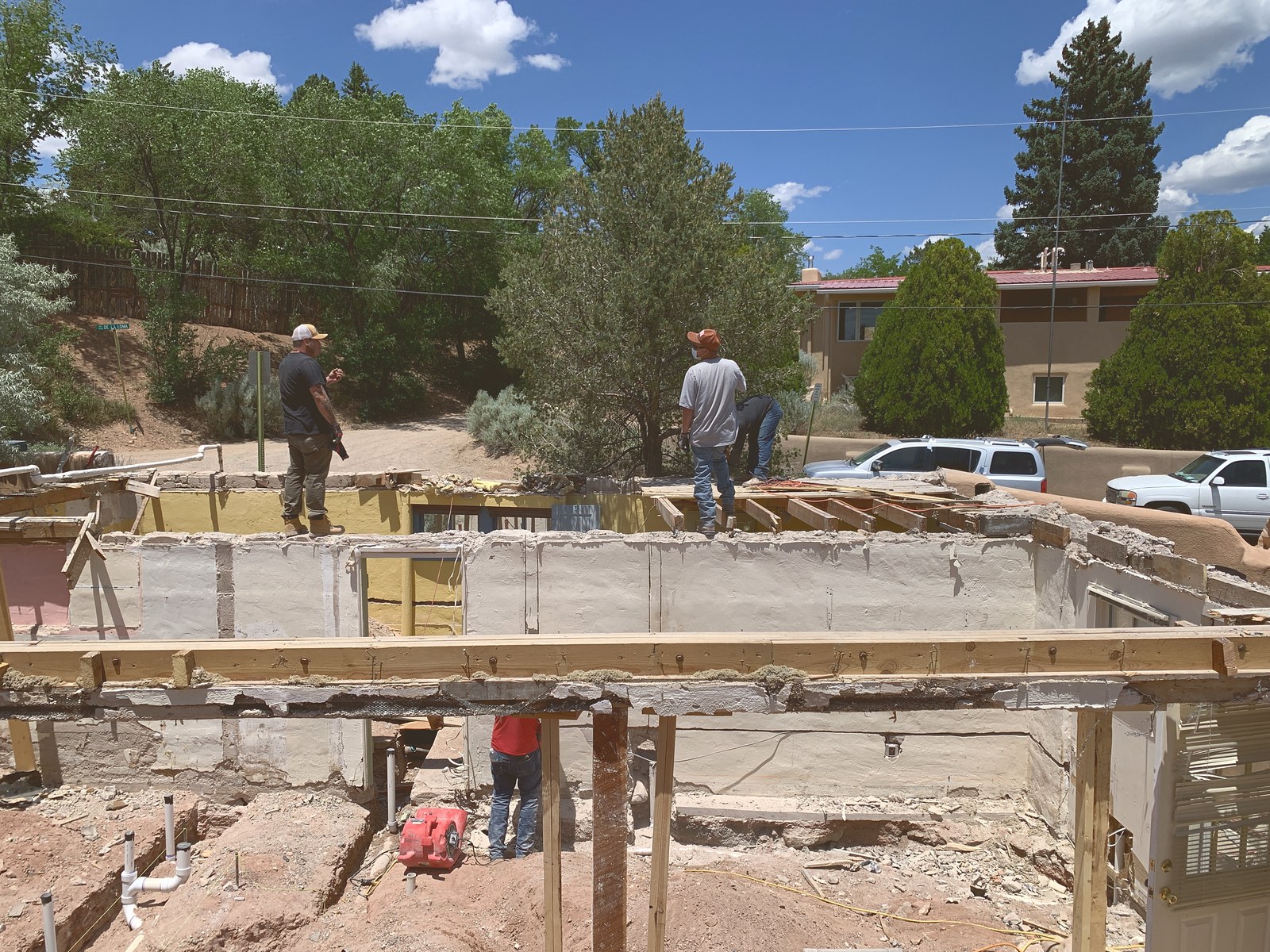 Summer 2020: four of the crew working along an open wall line, setting a long new timber beam, with the neighbouring rooftops and trees behind them.