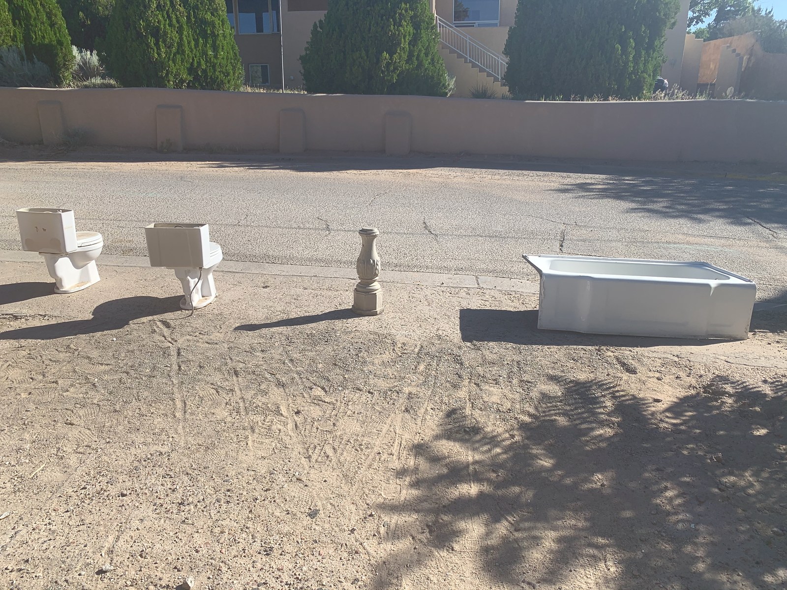June 2020: the old fixtures lined up on the verge waiting to go, two toilets, a tub and a pedestal basin, with the compound wall behind them.
