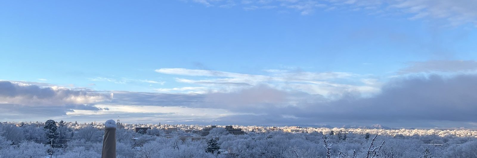 The whole of Santa Fe under fresh snow seen from the deck, every tree and rooftop white to the horizon under a wide blue sky.