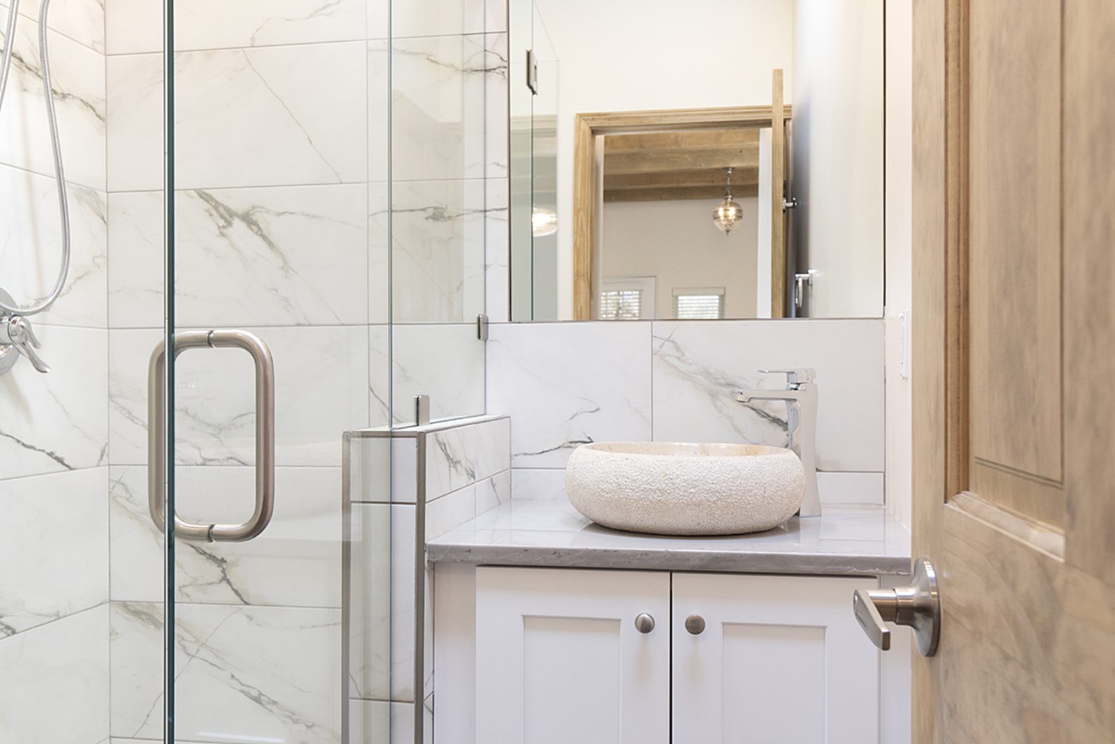 Unit A's bathroom with a glass shower enclosure, a vessel sink on a white vanity, and marble-look tile.