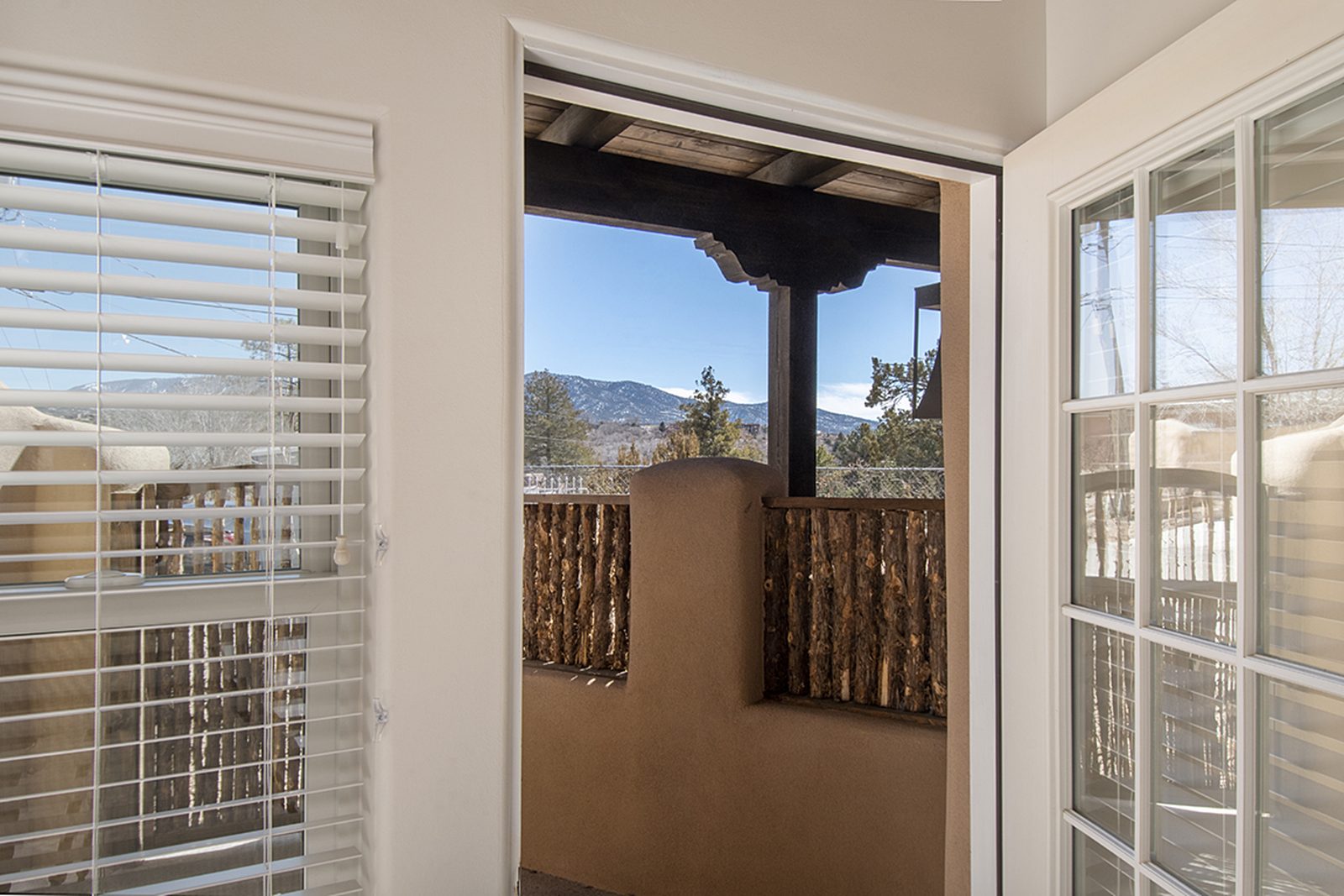 Looking out from inside Unit A through a window framed in wood, past the coyote fencing to the mountains.