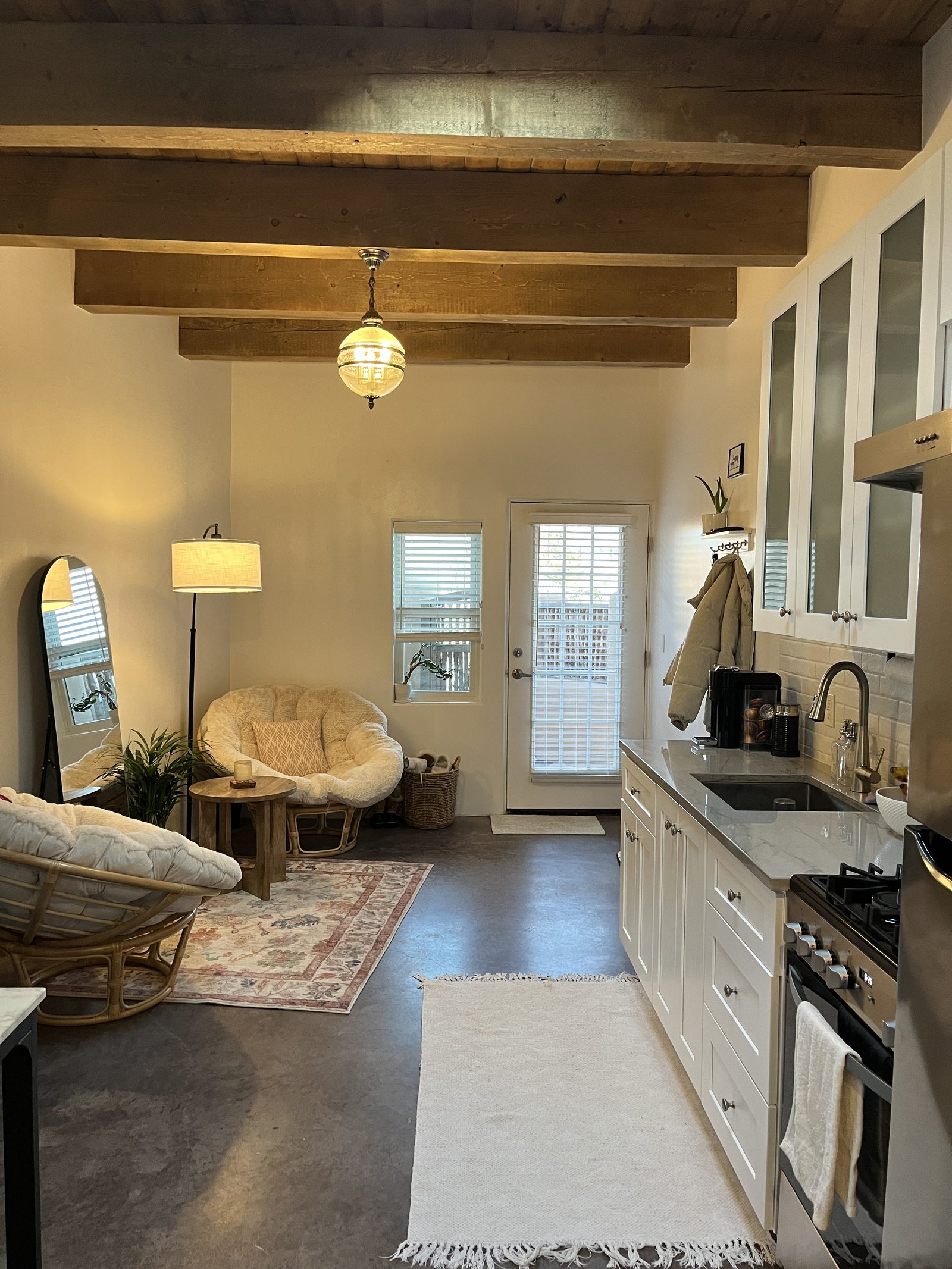 Unit A in the evening: two papasan chairs under a warm pendant light, concrete floors, and the kitchen glowing along the right wall.