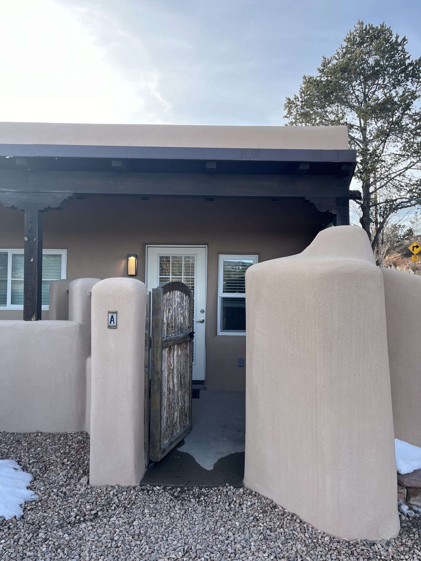 Unit A's coyote-pole gate standing open in winter, an A plaque on the plastered pillar and the covered portal behind.