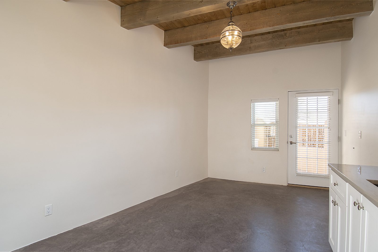 Unit A's living space looking toward the entry, wood-beamed ceiling above finished concrete floors.