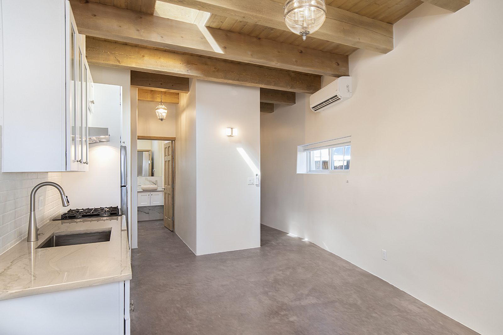 Unit A's great room, light and open, with a viga-and-latilla wood ceiling, a pendant light, and a doorway through to the kitchen.