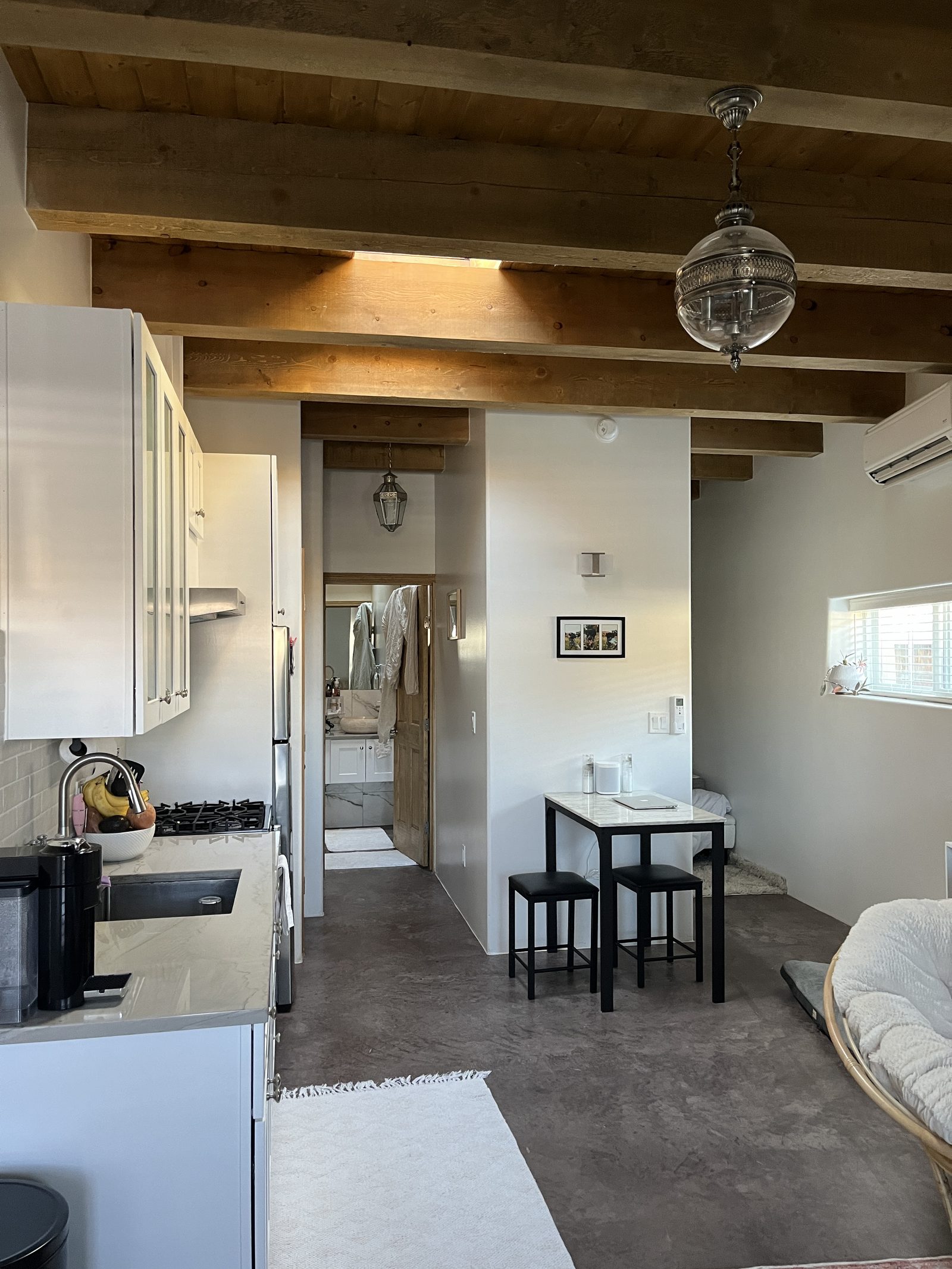 Unit A as a tenant lives in it: white kitchen with gas range down one side, a marble bistro table under the beams, and the bathroom beyond.