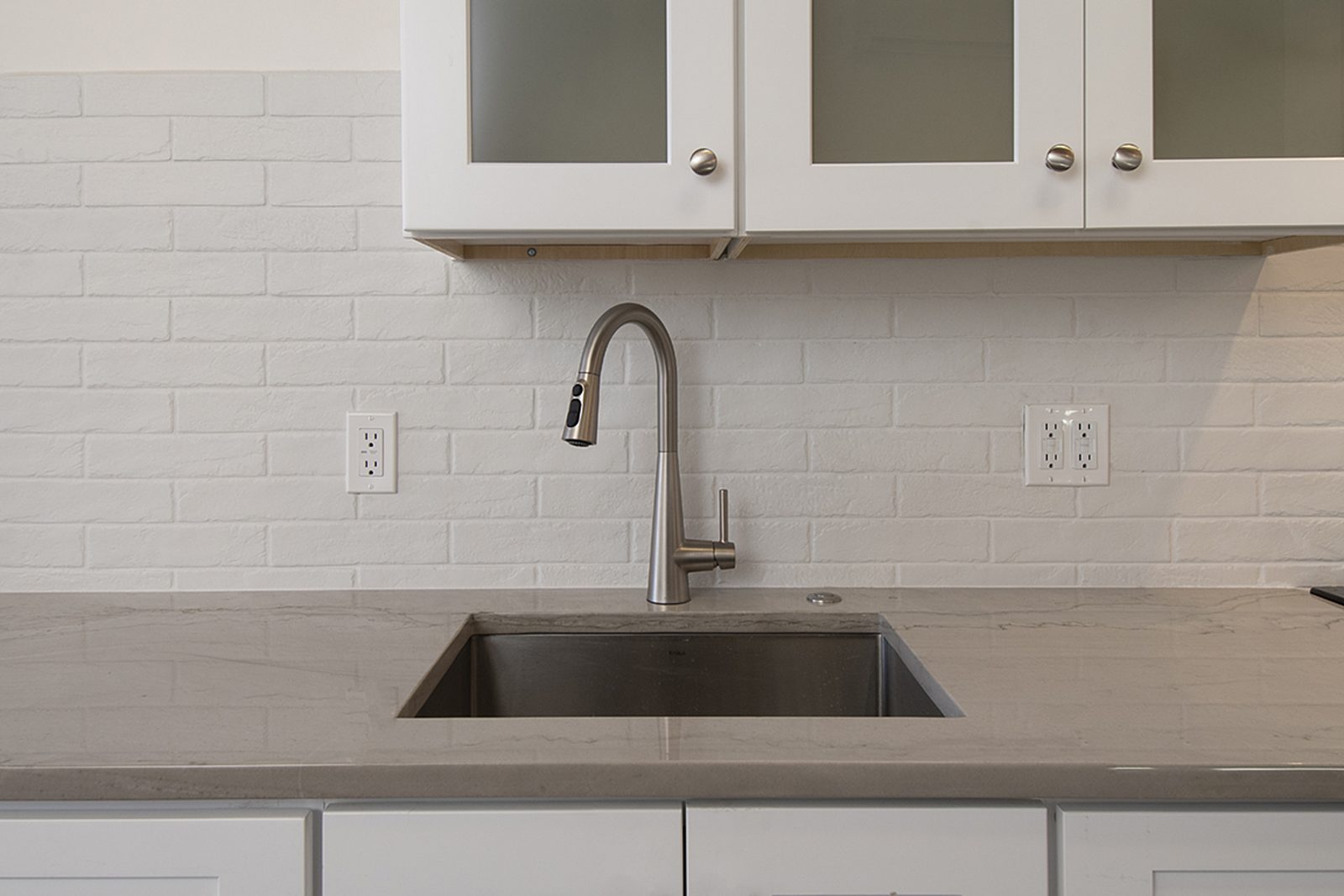 Close view of Unit A's kitchen counter, a deep stainless sink and a white subway tile backsplash.