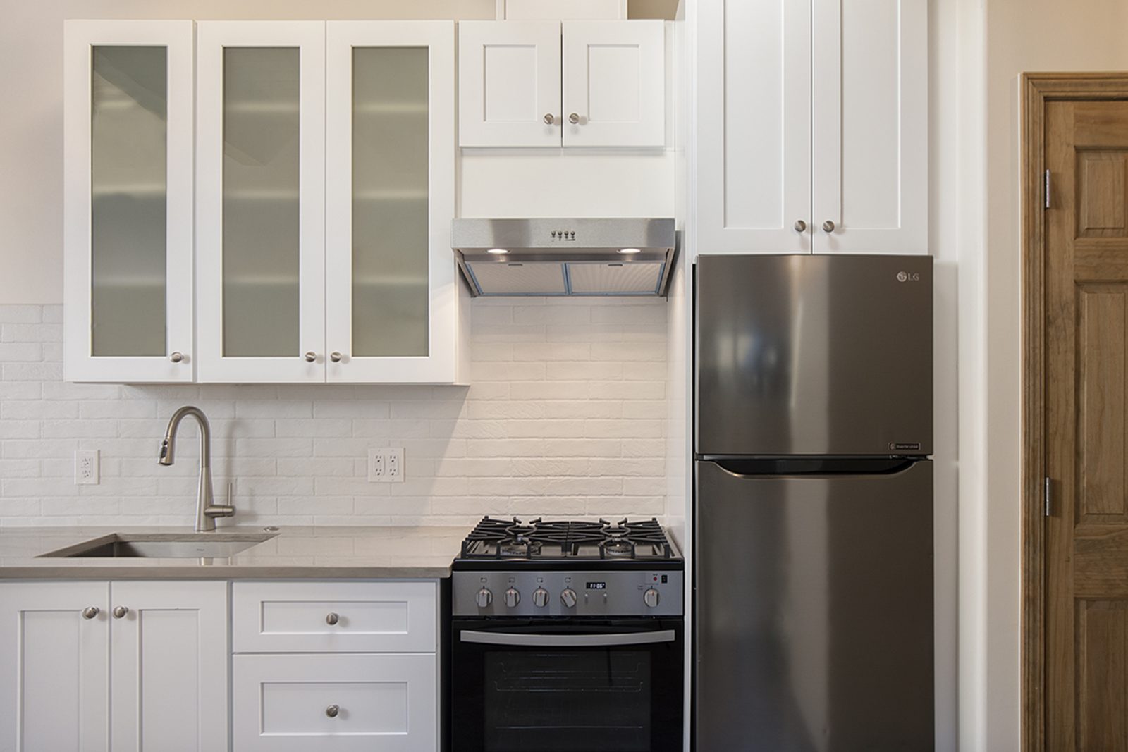 Unit A's kitchen: white shaker cabinets with glass fronts, a gas range, a stainless fridge, and a wood-beamed ceiling.