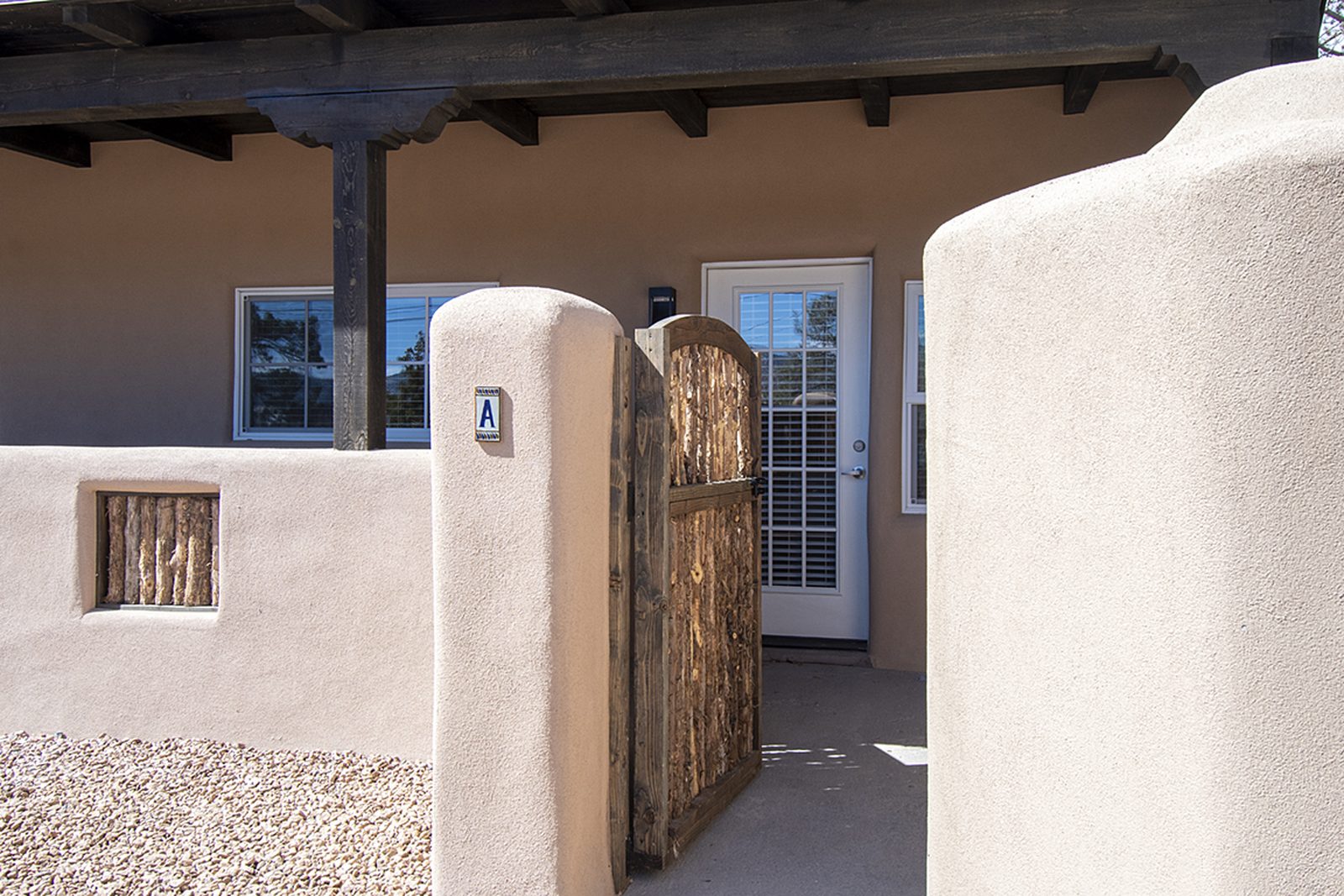 Unit A's private entry: a stuccoed wall with a coyote-pole gate opening onto a covered portal with French doors.