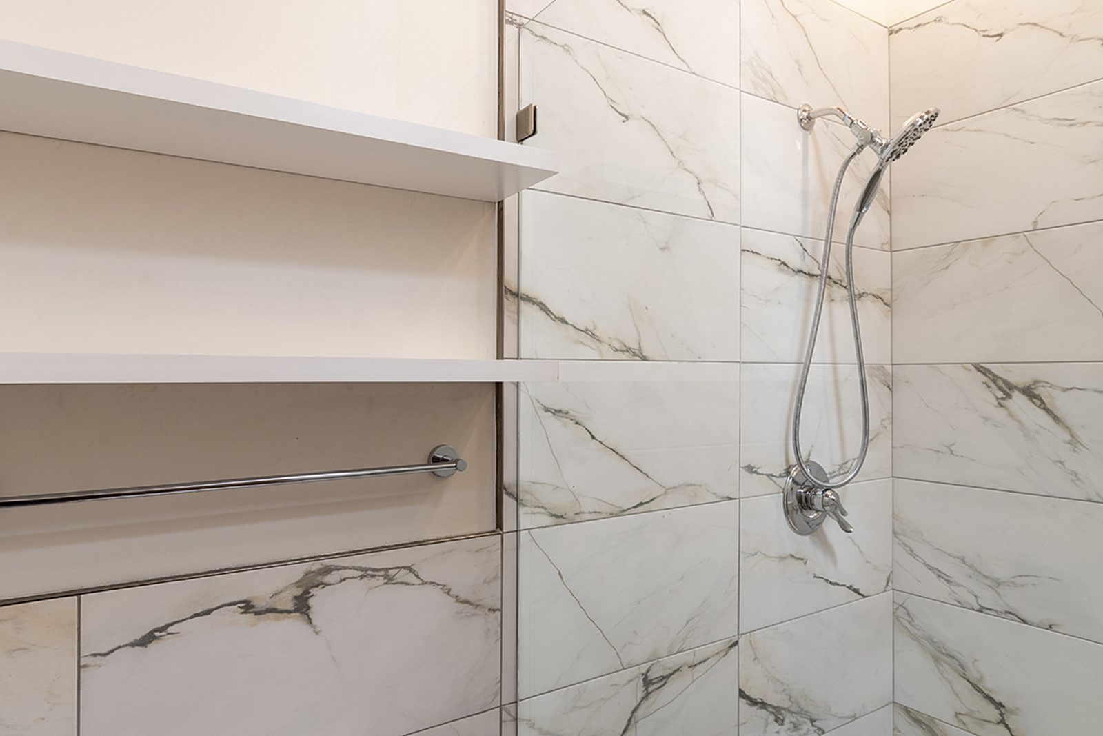 Unit A's walk-in shower, tiled floor to ceiling in marble-look porcelain with a recessed shelving niche.