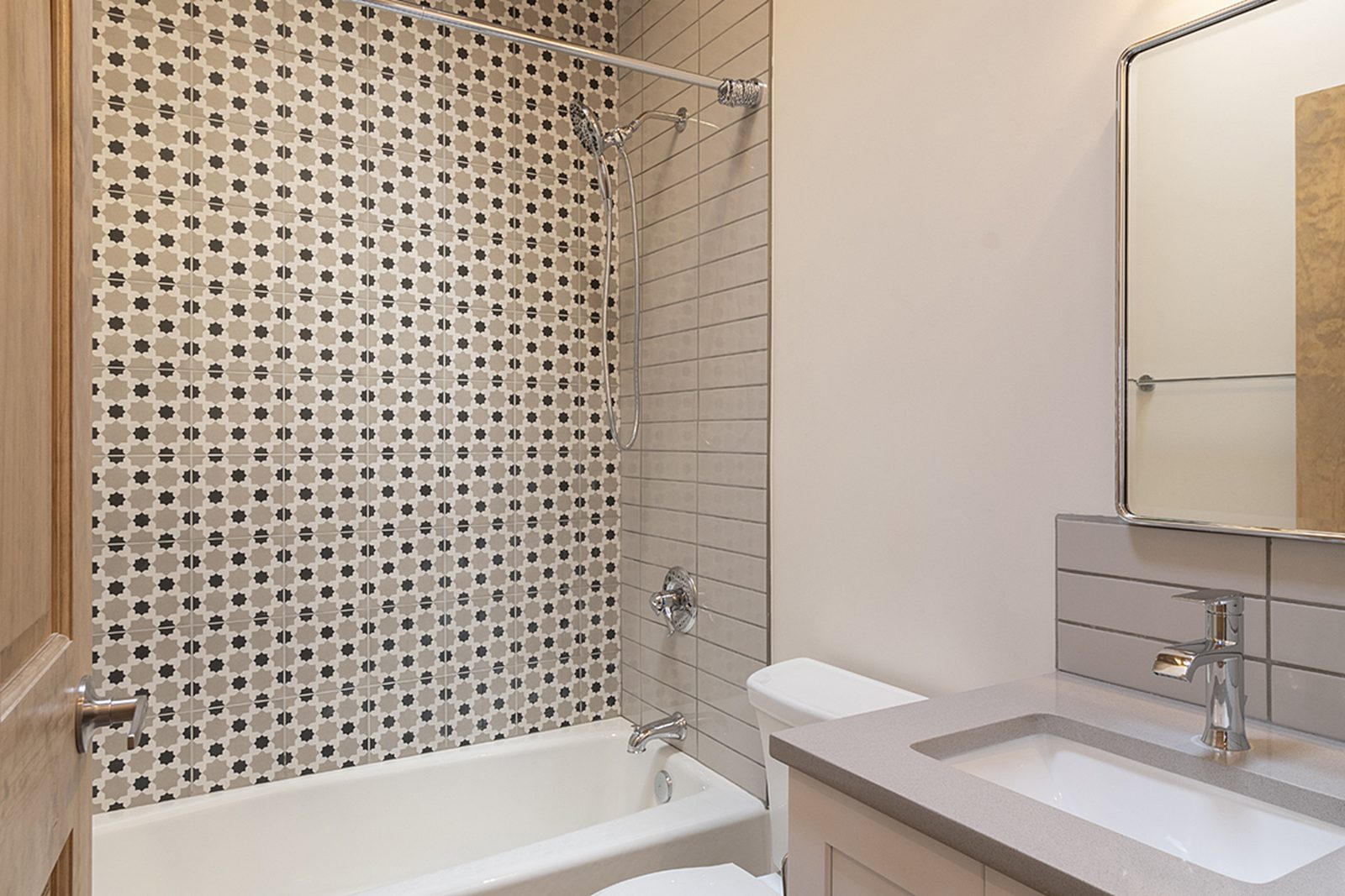 Unit B's second full bathroom with a tub, a patterned tile surround and a white vanity.