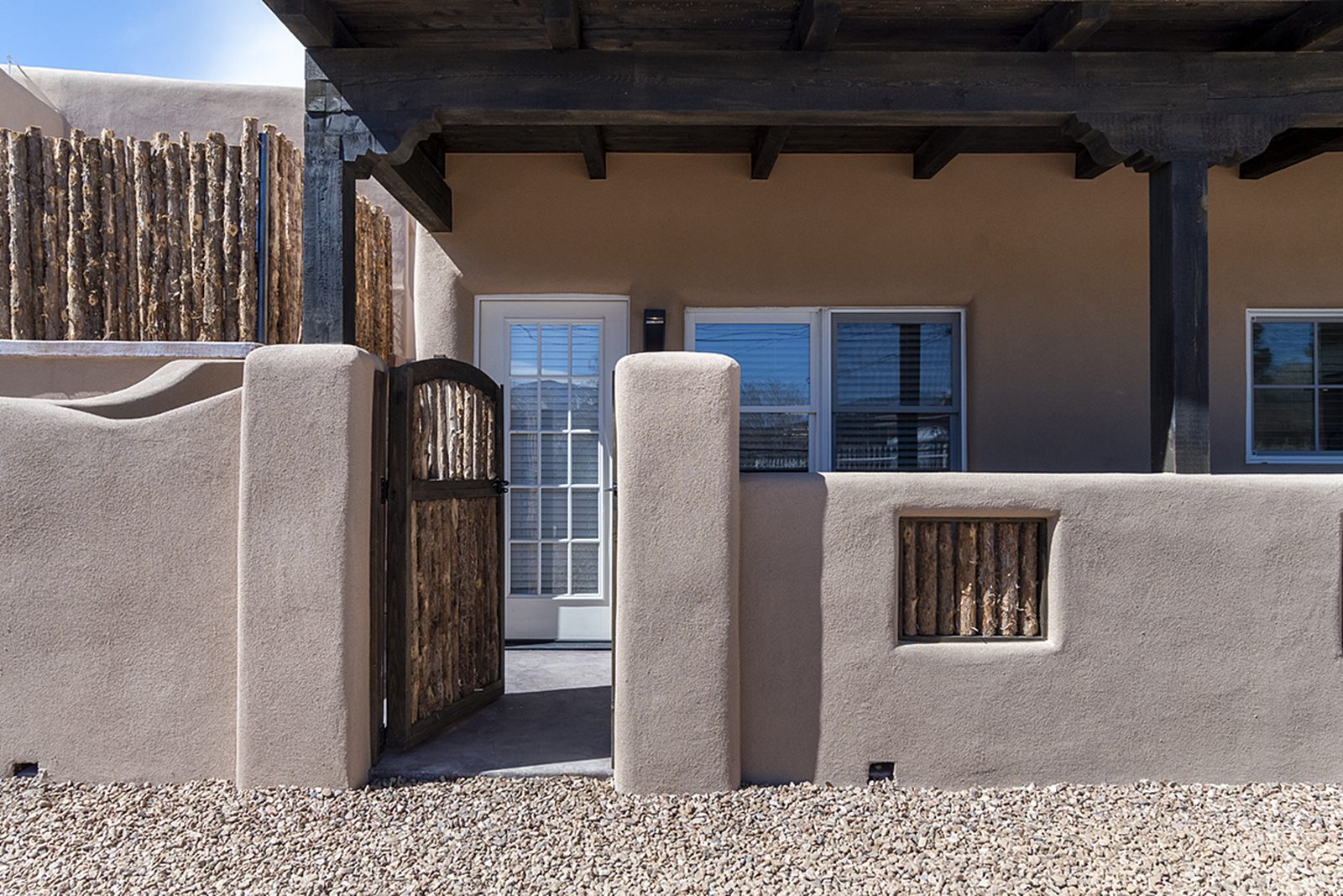 Unit B's entrance: a coyote-pole gate in a curved stucco wall under a beamed portal.
