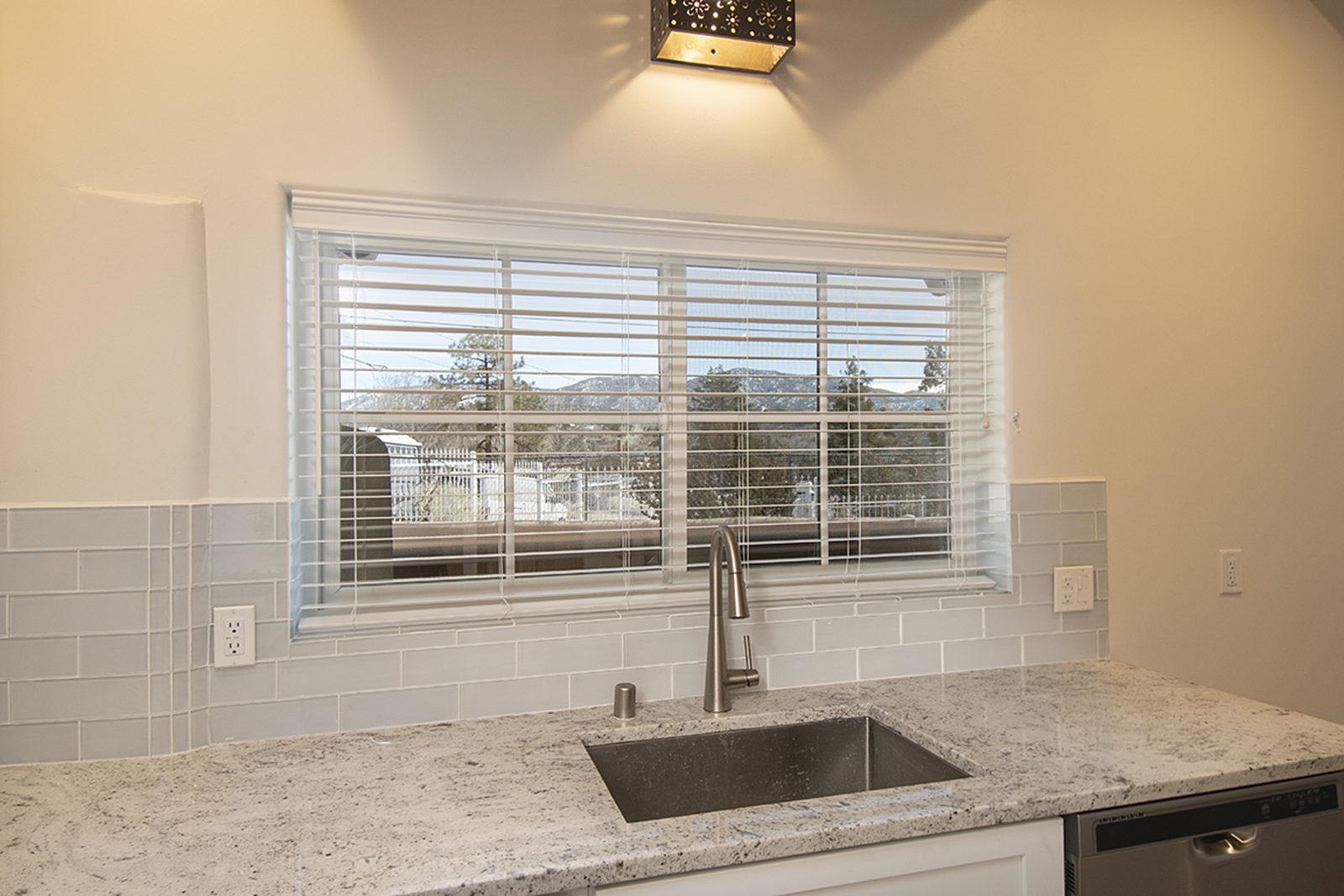 Unit B's kitchen sink set under a window looking out to the trees, with granite counters and a tiled backsplash.