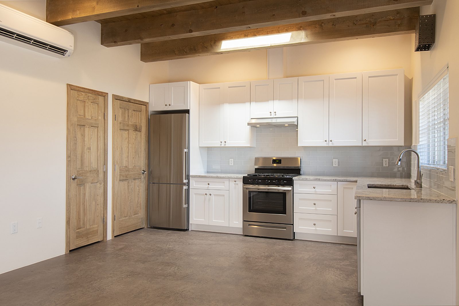 Unit B's kitchen: white cabinets, a stainless gas range and fridge, finished concrete floors, and a wood door through to the hall.