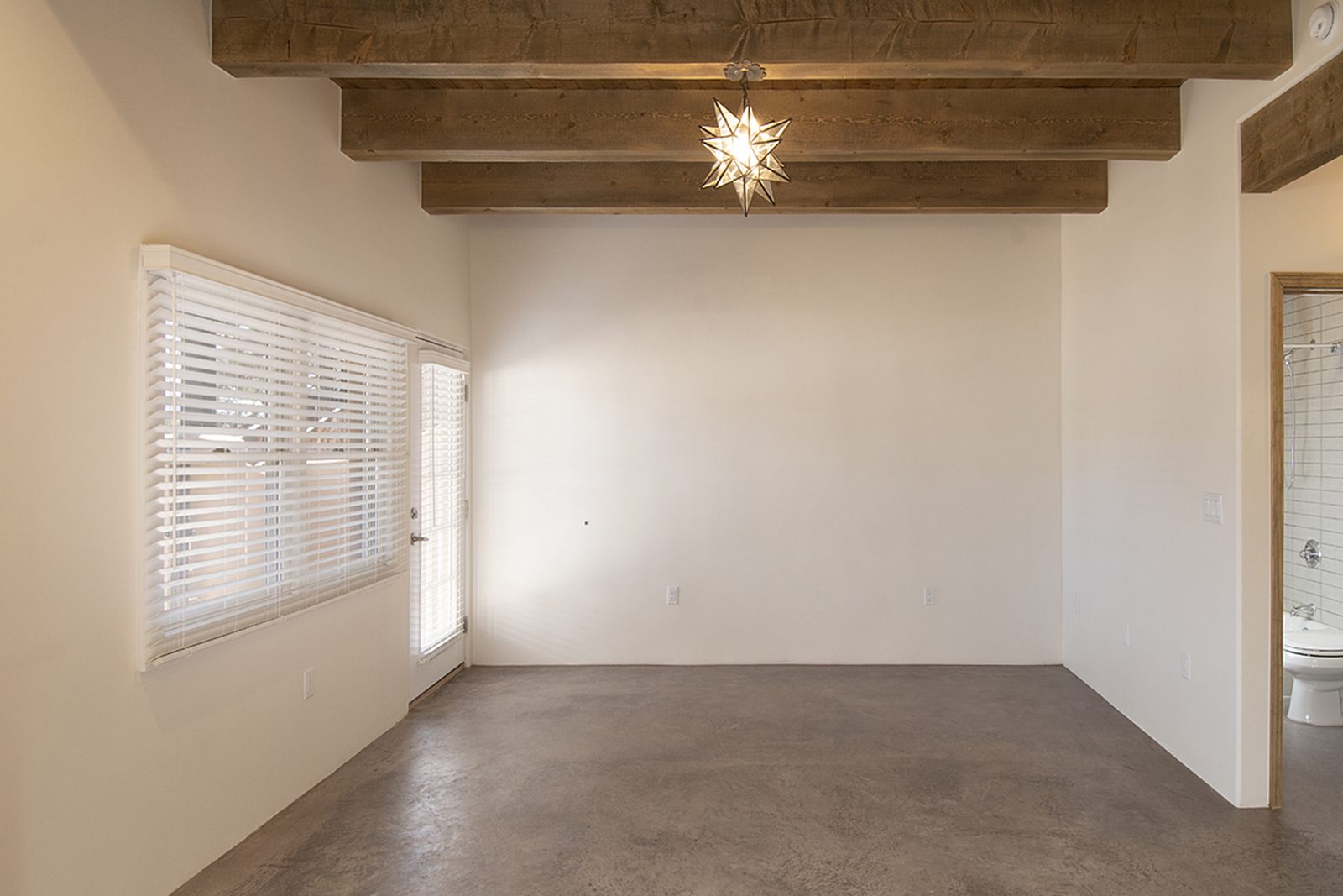 Unit B's living room with exposed beams, a star pendant light and a window over concrete floors.