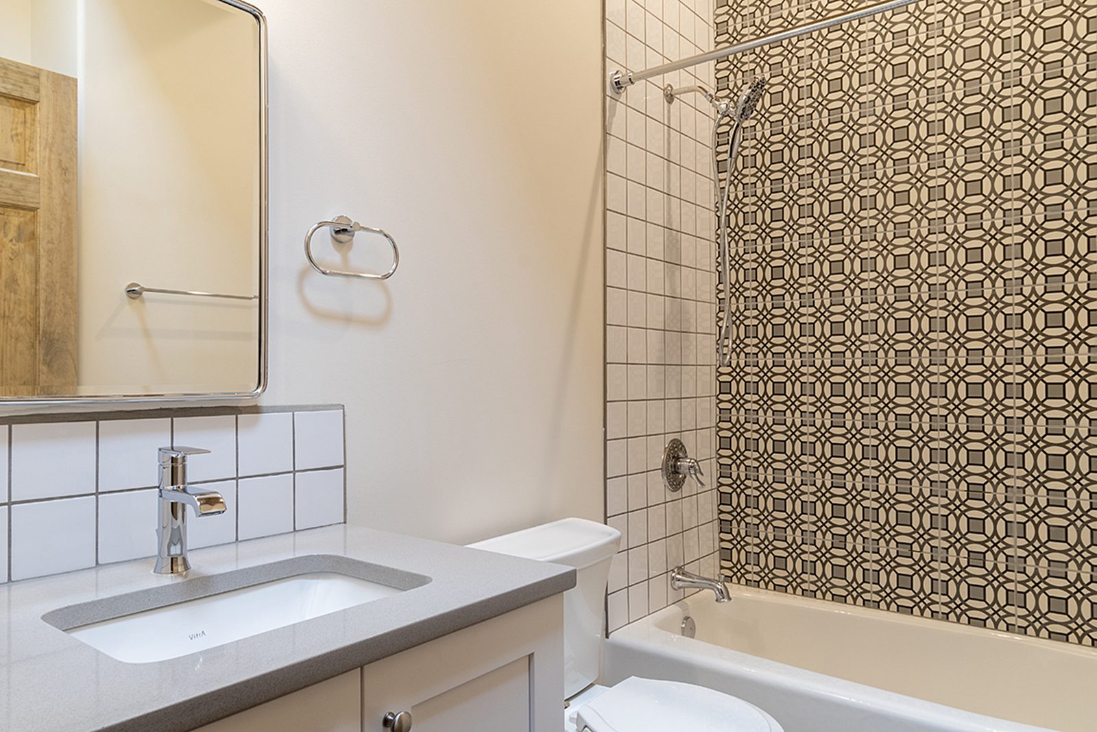 Unit B's primary bathroom: a white vanity, a framed mirror, and a tub set against a patterned tile wall.