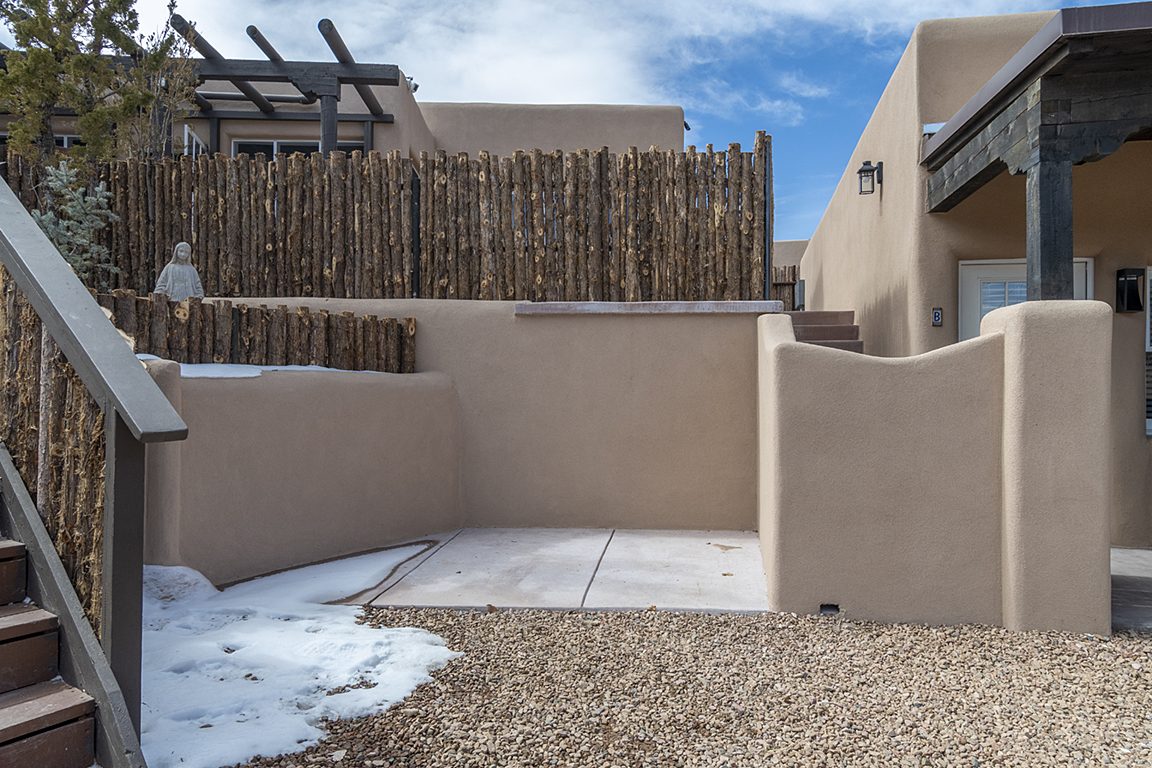 Unit B's walled side patio: fresh plaster, a coyote-pole fence above, a St Francis statue watching from the wall and steps up to the door.