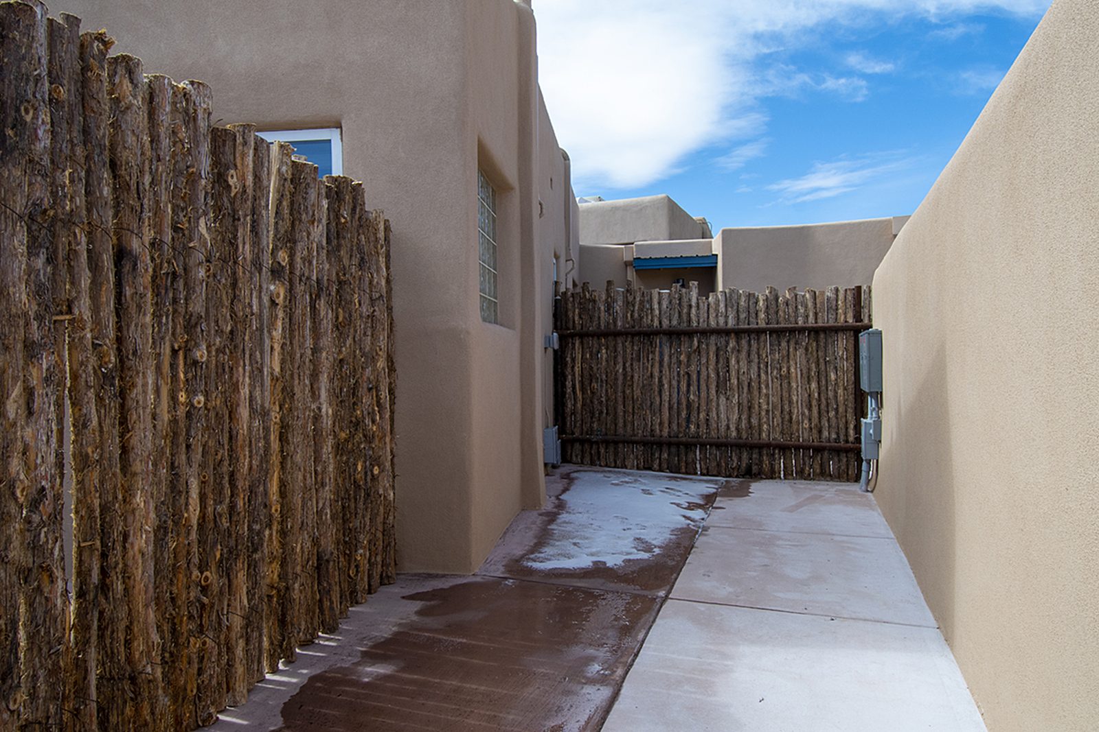 Unit B's side patio, a private run of concrete between stucco walls and coyote-pole fencing.