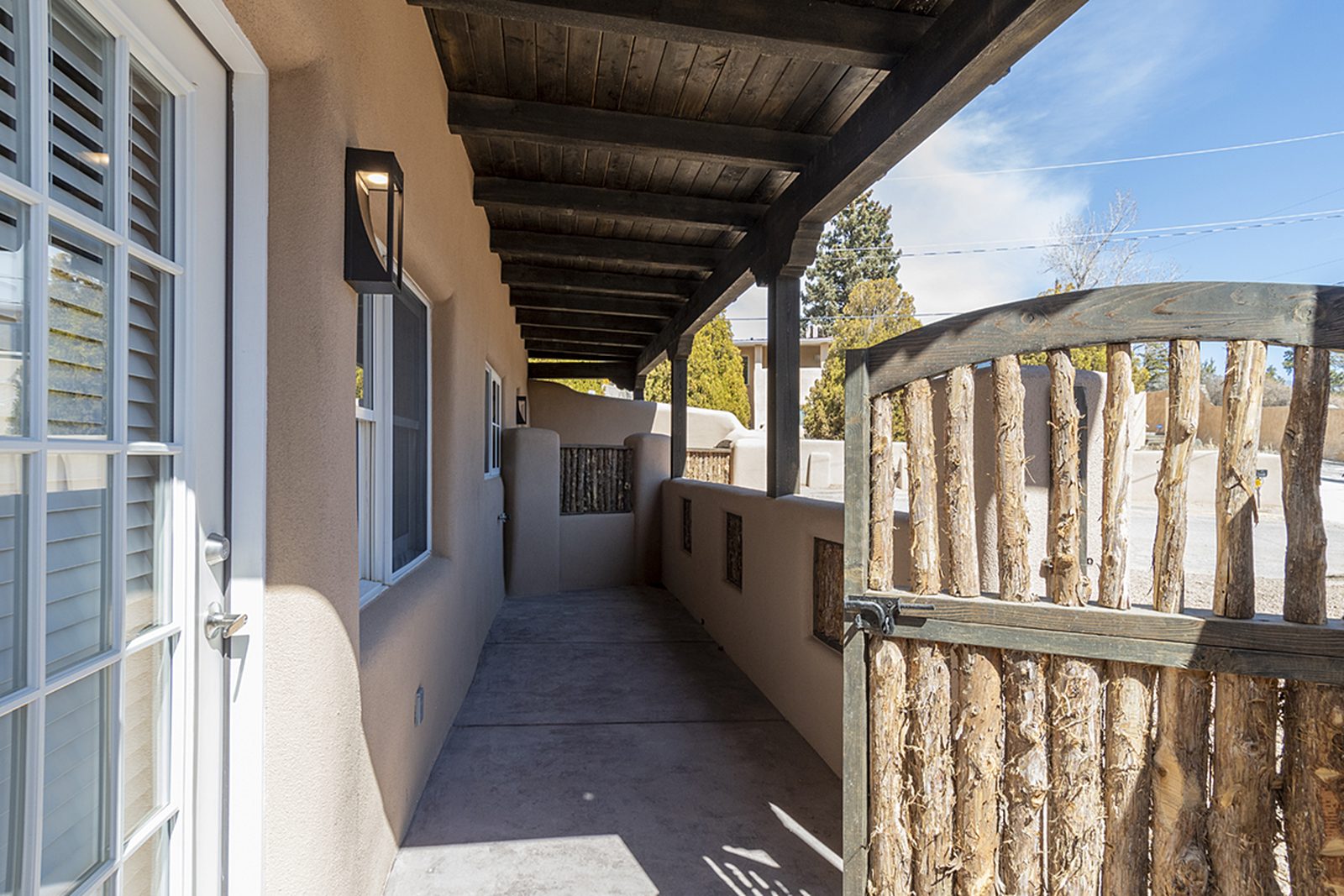 The portal outside Unit B, French doors under a beamed roof beside coyote-pole fencing.