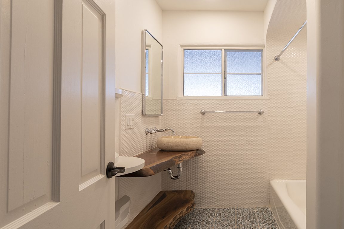Unit C's hall bath: penny-tile walls, a stone vessel sink on a live-edge walnut slab, and patterned tile underfoot.