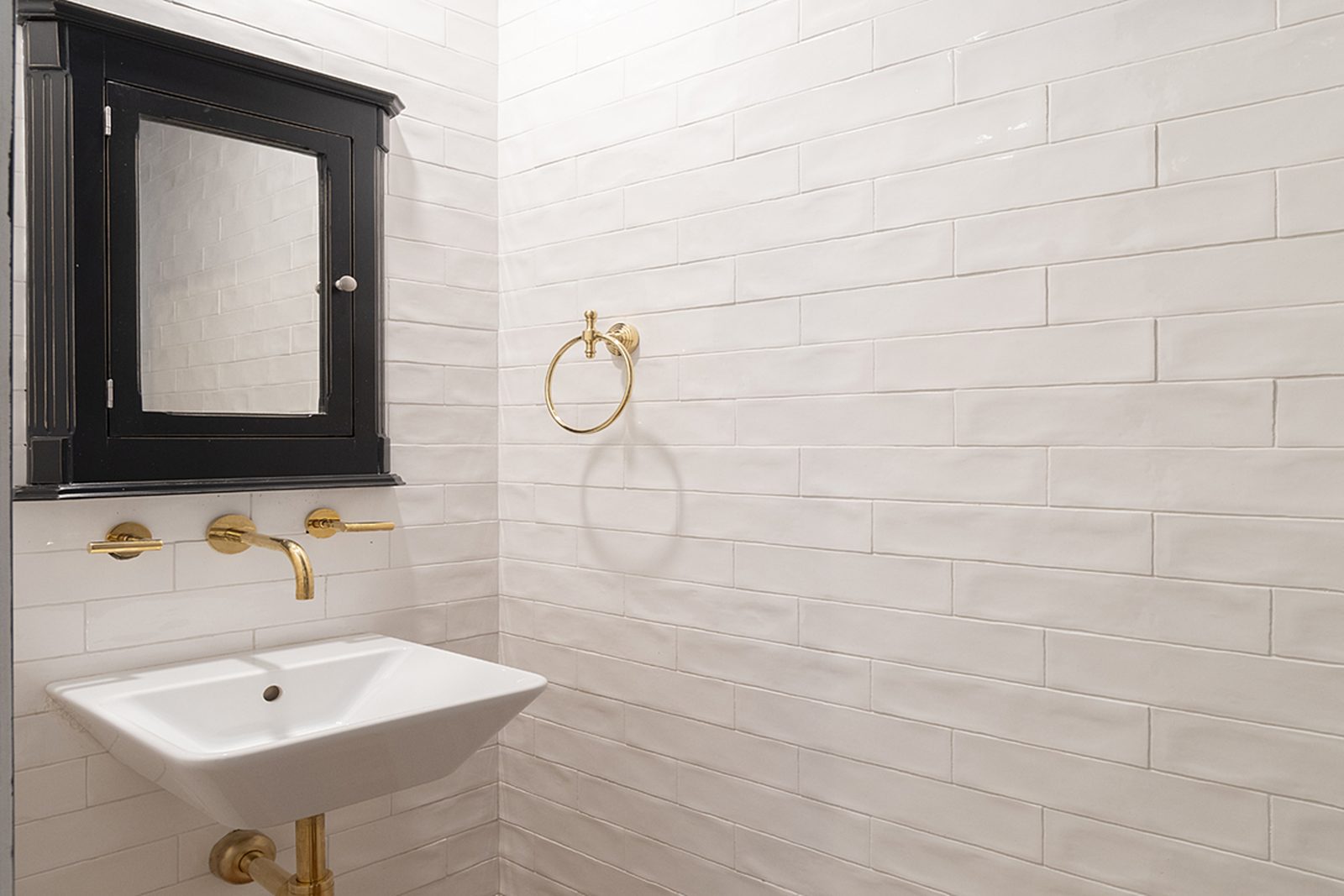 Unit C's bathroom with a wall-mounted sink, a black-framed medicine cabinet and white tile.