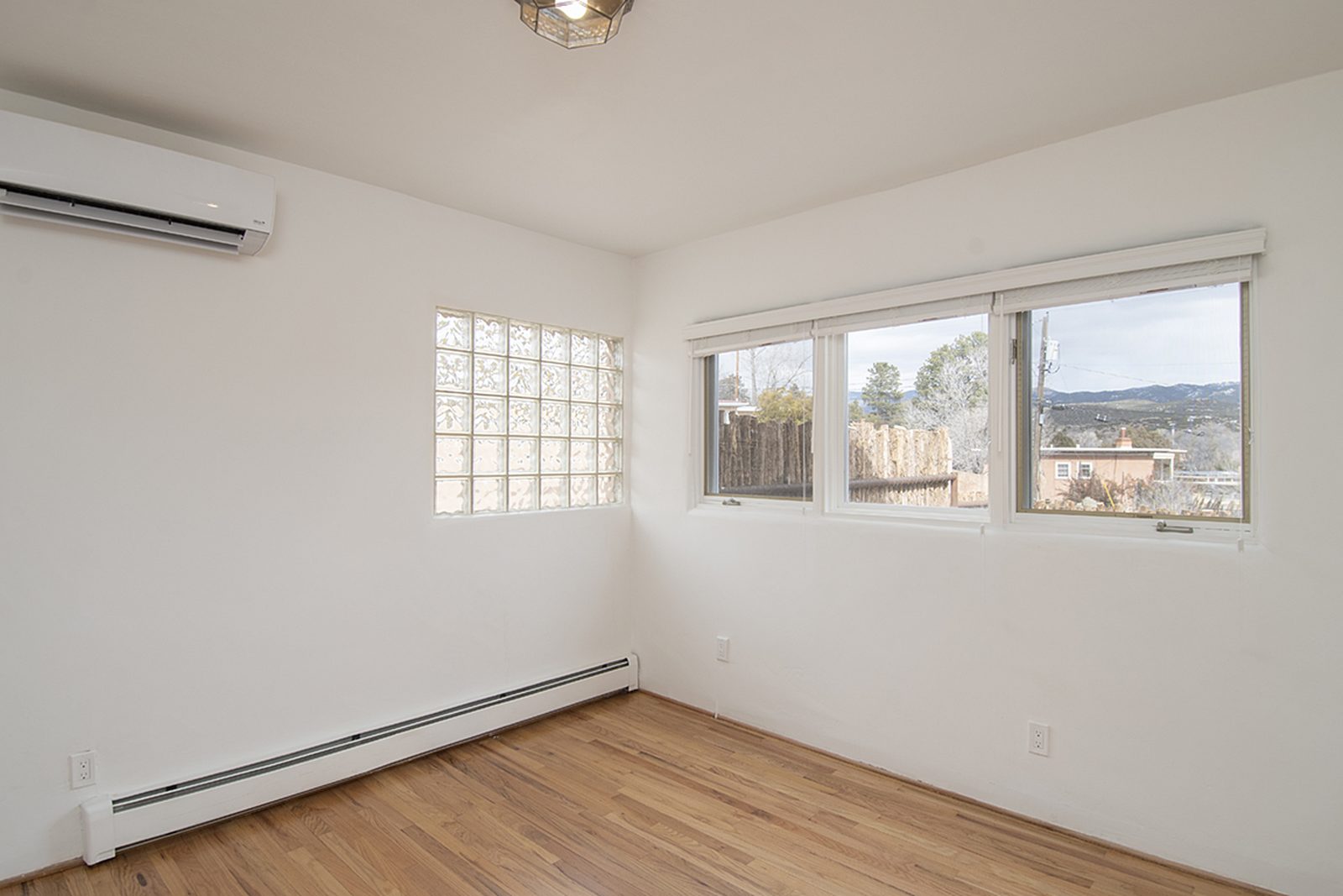 Unit C's first bedroom with hardwood floors, a window looking out to the trees, and a mini-split unit.