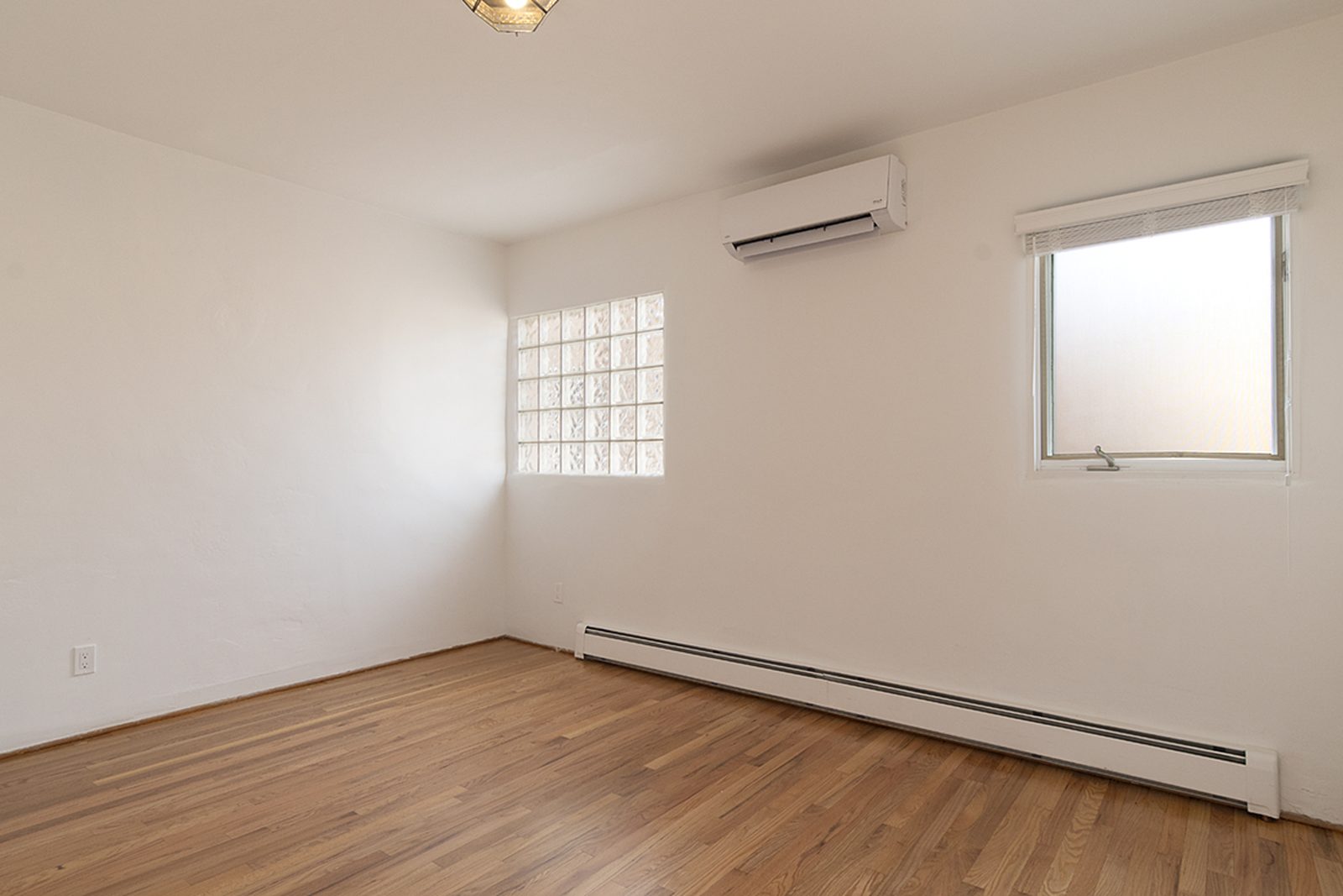 Unit C's second bedroom with hardwood floors and windows on two walls.