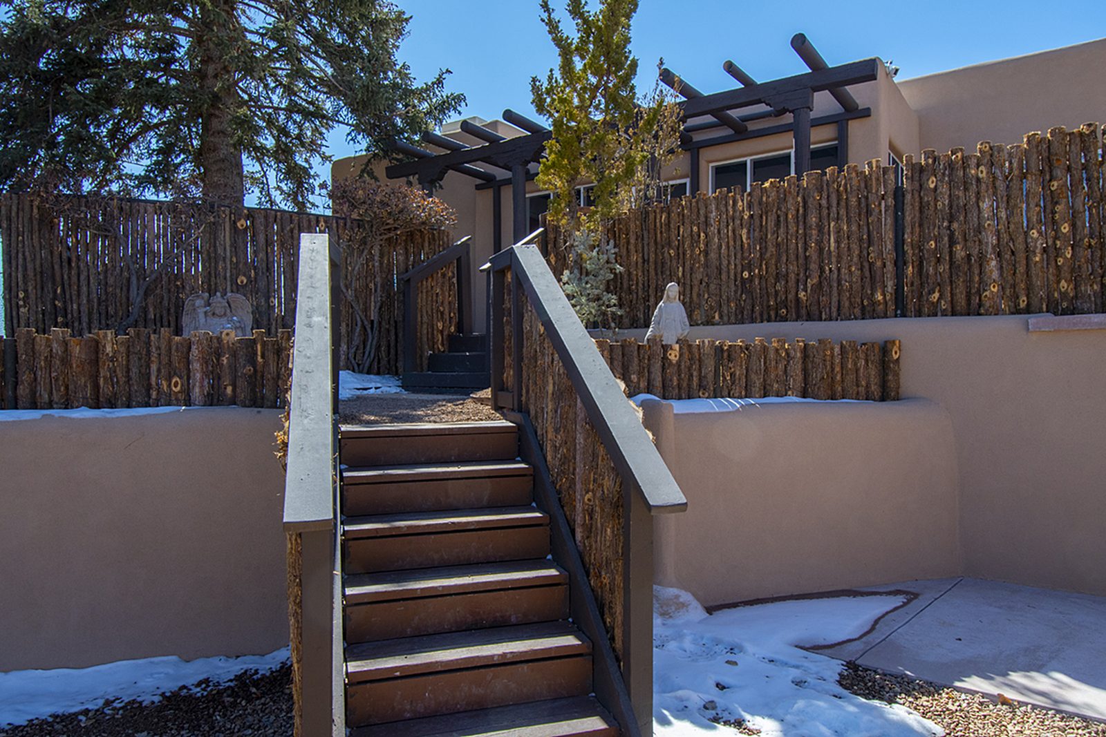 Unit C seen from its own yard: stuccoed walls, a pergola along one side, and a stacked woodpile.