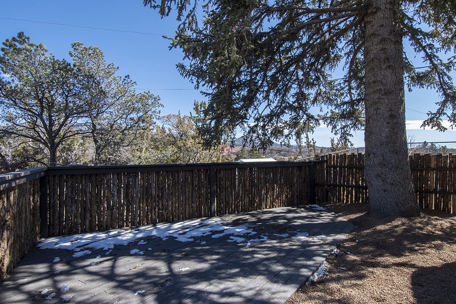 Unit C's front yard under a large evergreen, enclosed by coyote-pole fencing with the valley beyond.