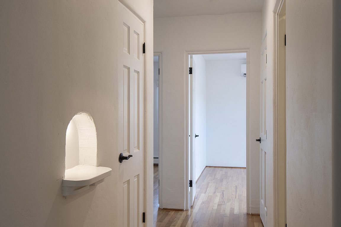 Unit C's hallway: hand-plastered walls, a lit nicho shelf, and doorways opening to the bedrooms off both sides.