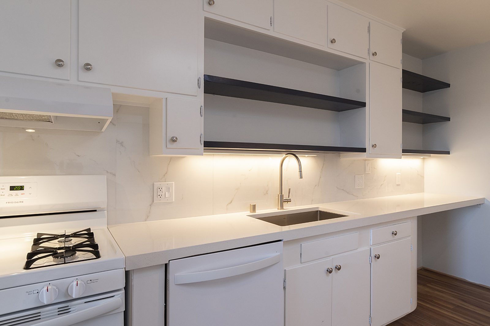 Unit C's kitchen from the range end, with a gas cooktop, a deep sink and open shelving above.