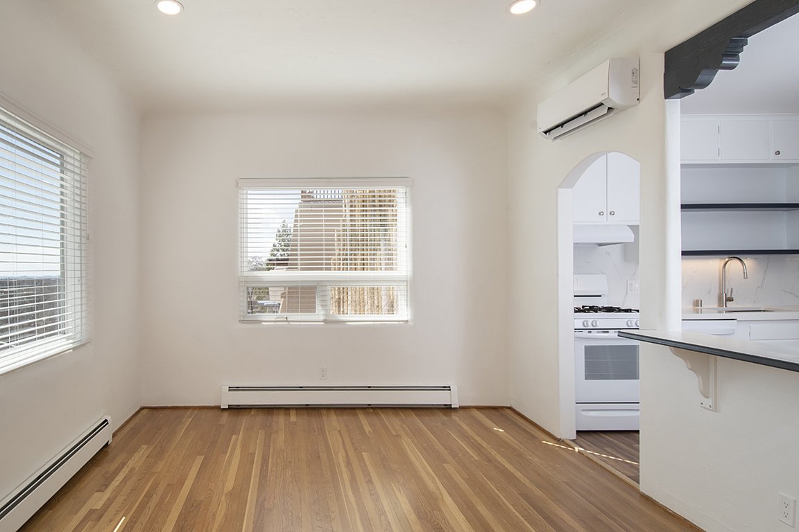 Unit C's great room, empty and full of light: refinished wood floors, an arched doorway into the white kitchen with a gas range, and a breakfast bar with open shelving.