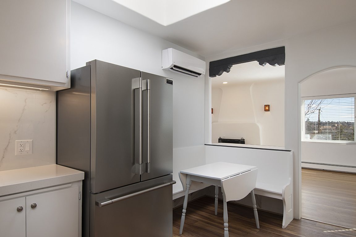 Unit C's breakfast nook: a built-in white bench and drop-leaf table beside the stainless fridge, through an arch from the great room.