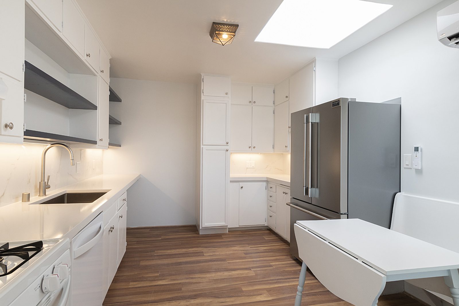 Unit C's kitchen: white counters, open shelving, a skylight overhead and a large stainless refrigerator.