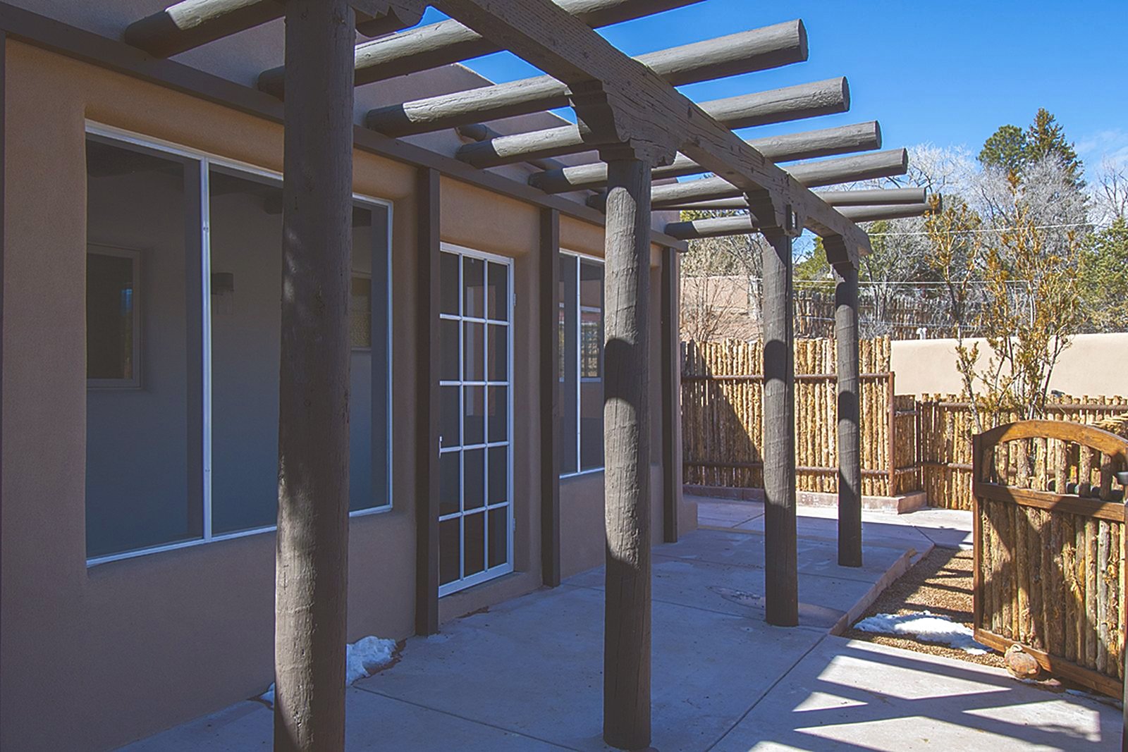 The front of Unit C: a timber pergola on heavy round posts running the length of the facade, tall windows and a glazed door behind it, and a coyote-pole fence and gate to the right.