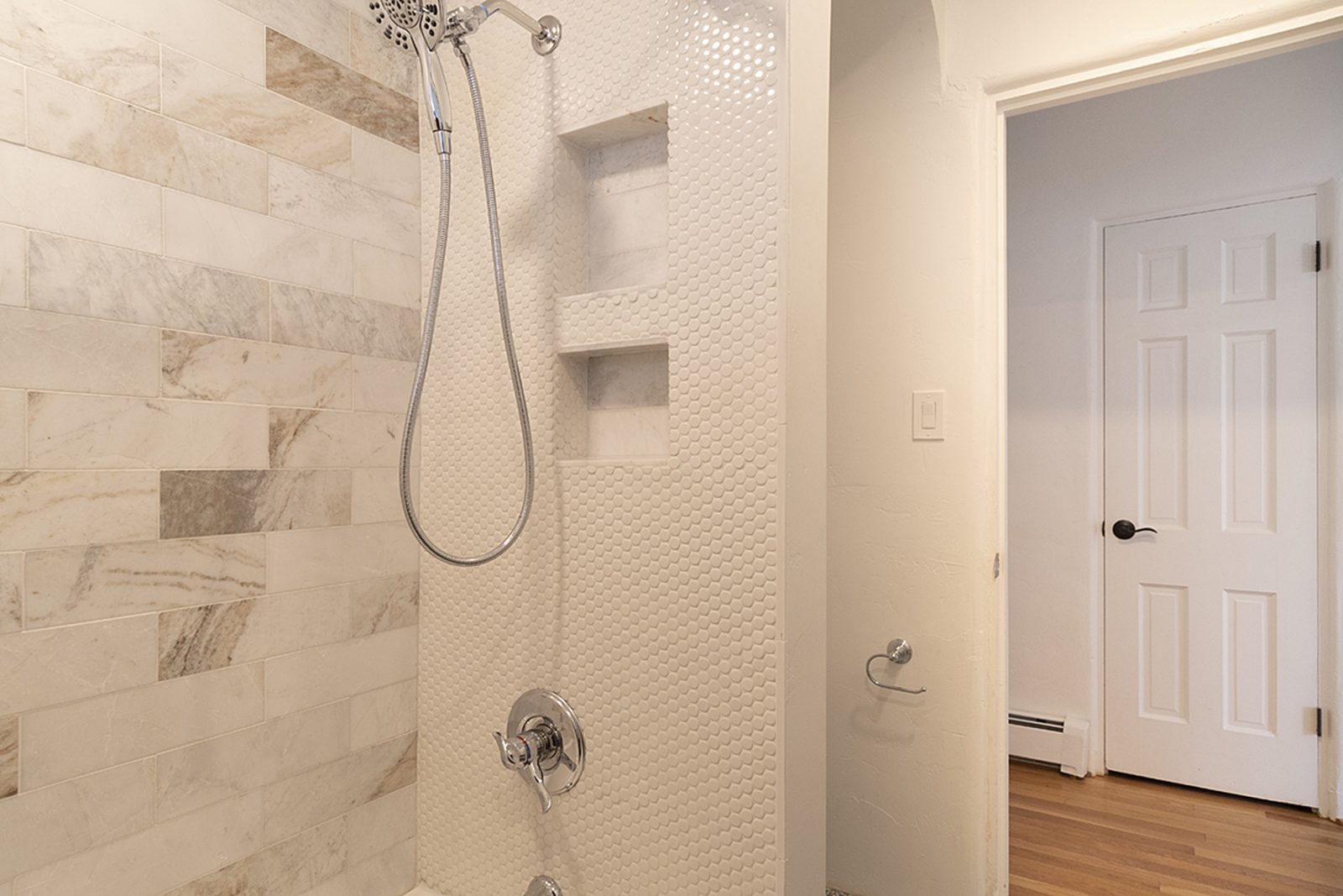 Unit C's half bath and shower, tiled in marble-look porcelain with a penny-tile floor.