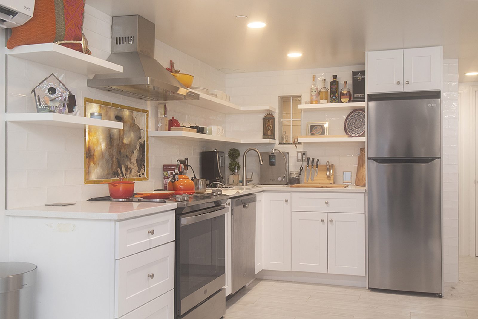 Unit D's kitchen: white cabinets, open shelving, a gas range and a stainless refrigerator.