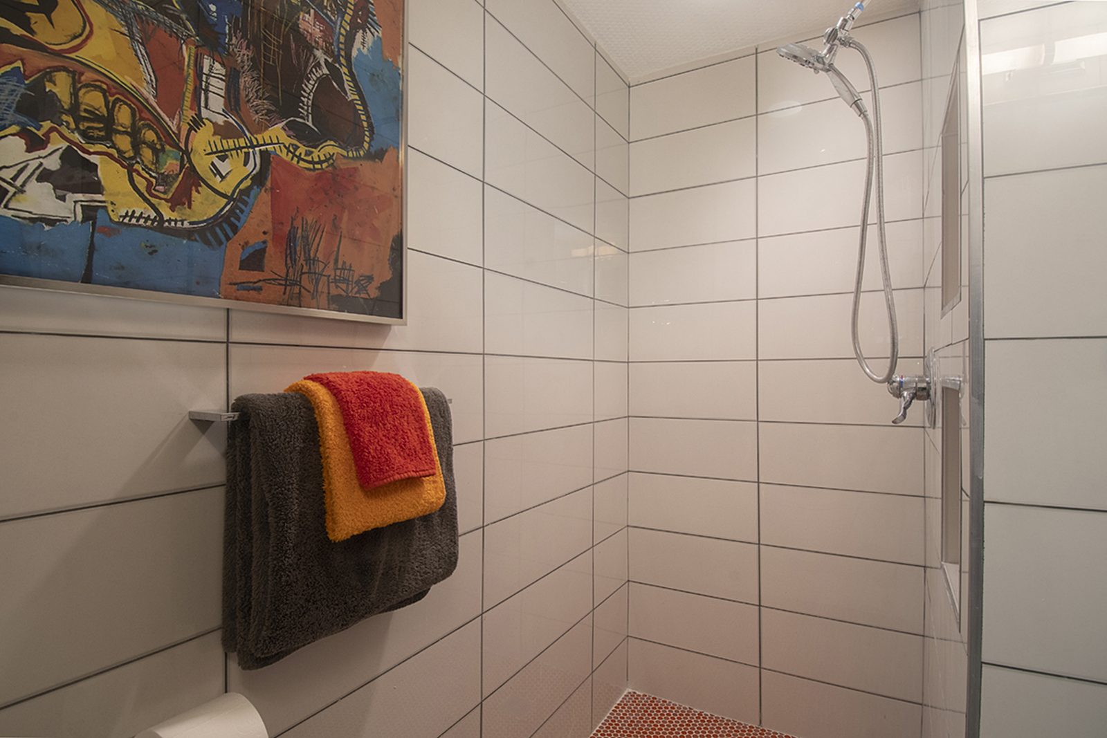 Unit D's walk-in shower, tiled in white with a fixed rain head.